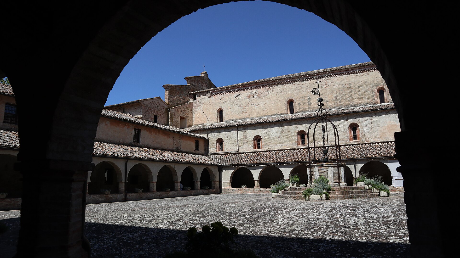 el claustro de la abadia de fiastra visto bajo un arco, con el pozo y el flanco de la iglesia