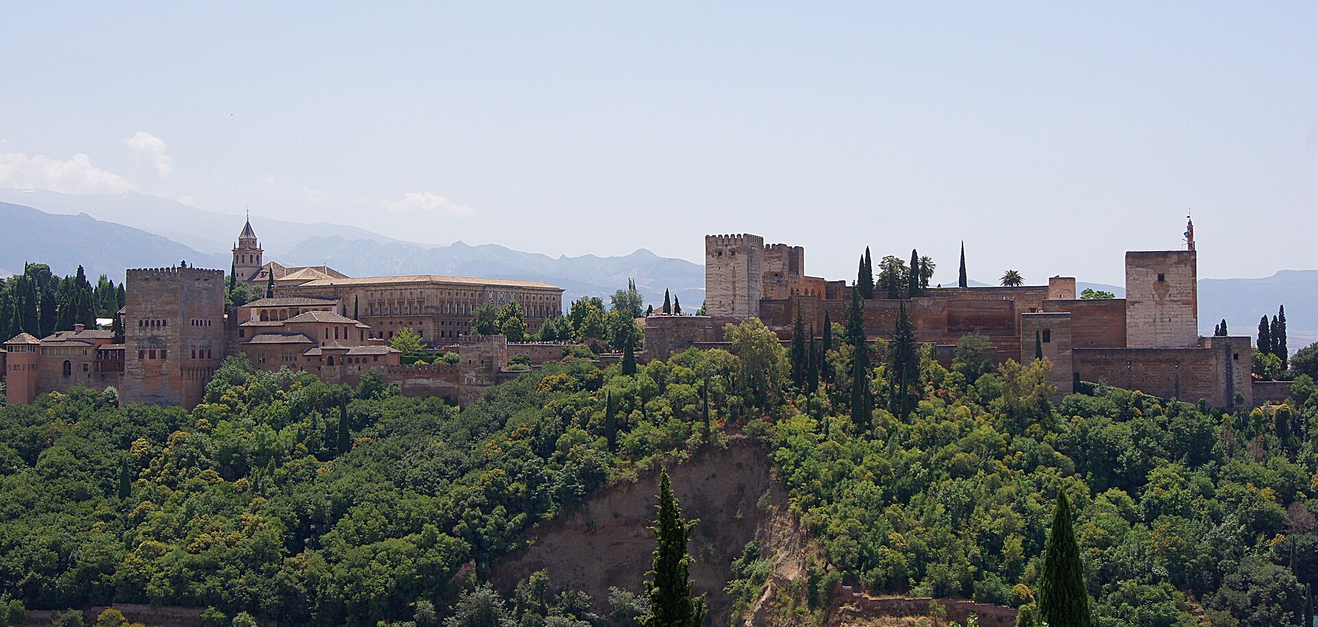l’alhambra sulla collina sopra granada vista dal mirador di san nicolas, con le torri rosse fra gli alberi e le montagne sullo sfondo