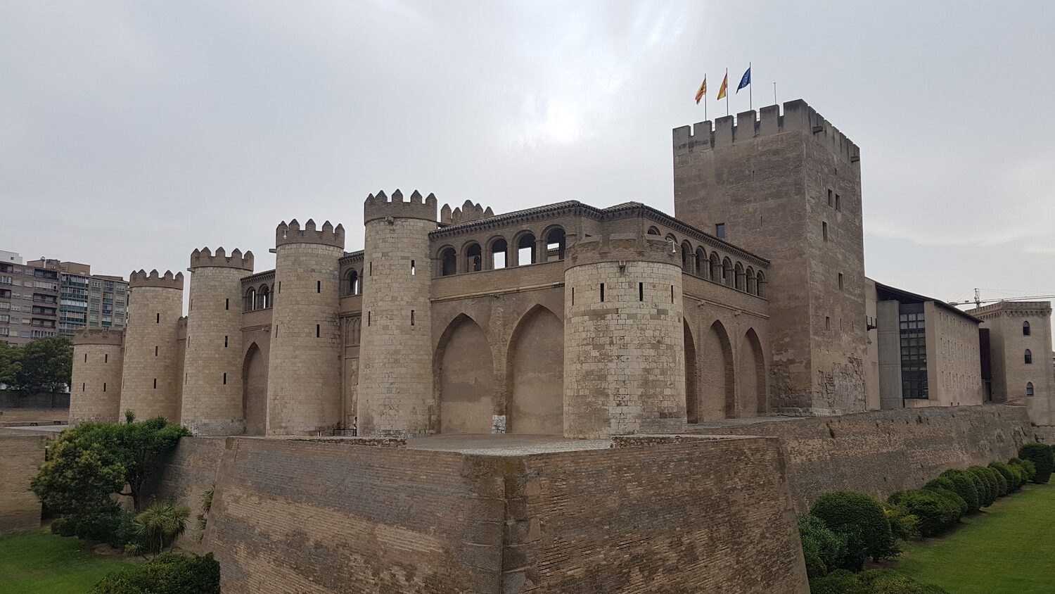 il palazzo dell’Aljafería di Saragozza visto di tre quarti, con le torri cilindriche merlate e la torre del Trovador sullo sfondo