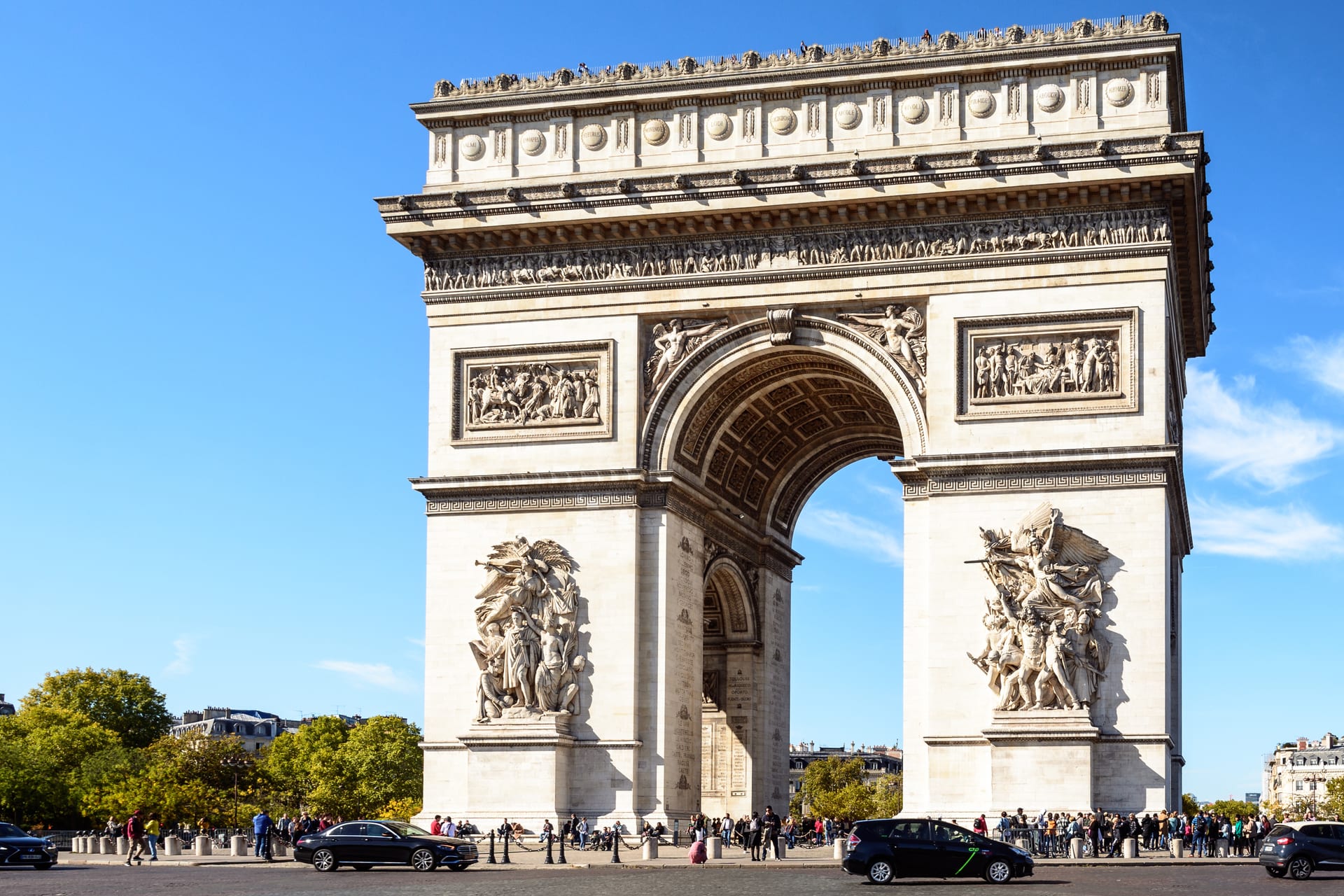 vista frontale dell arco di trionfo con i quattro rilievi scolpiti sui piloni, cielo azzurro, auto e persone ai piedi del monumento
