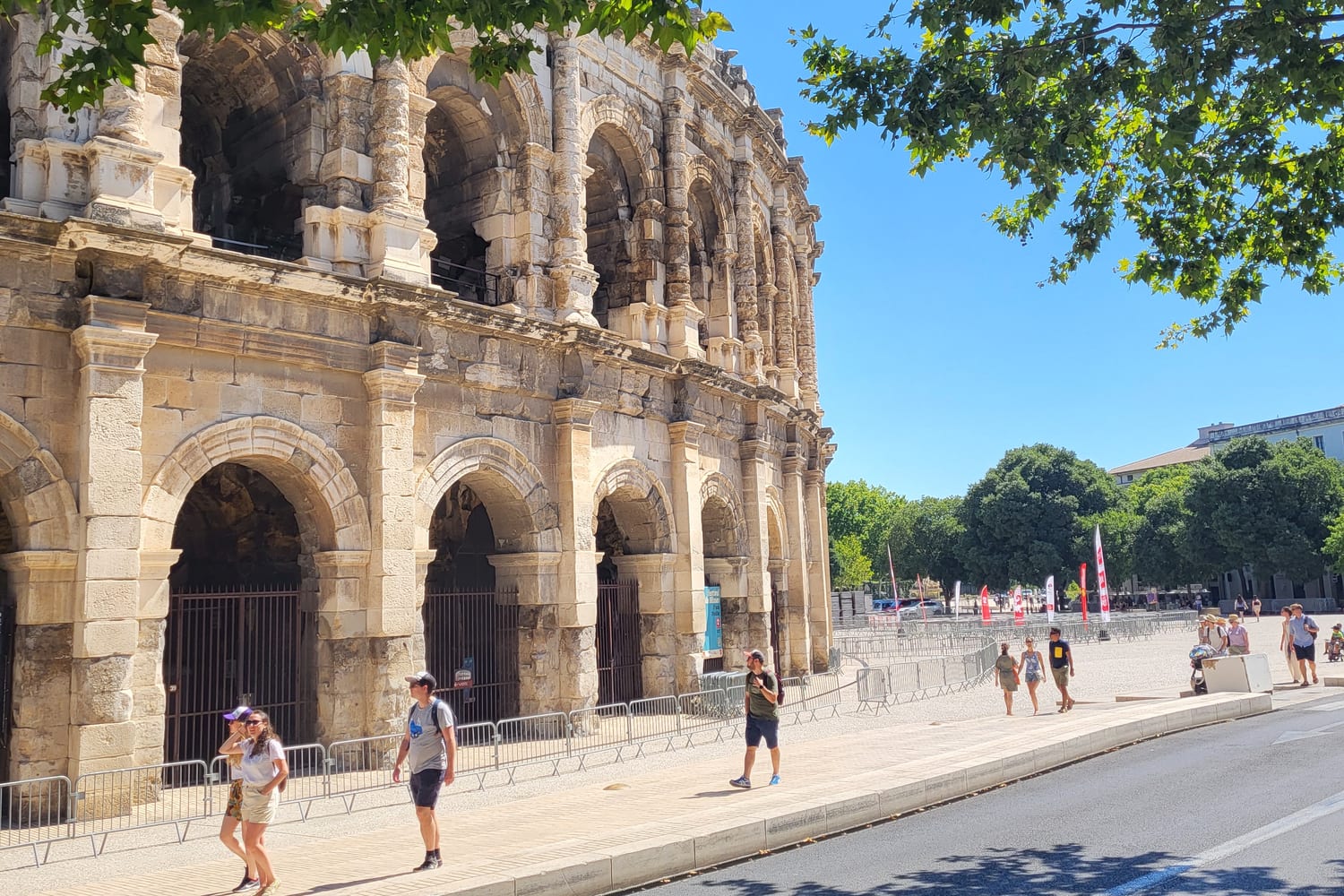 la fachada exterior de la Arena de Nimes con sus dos niveles de arcadas, vista desde la calle bajo los plátanos