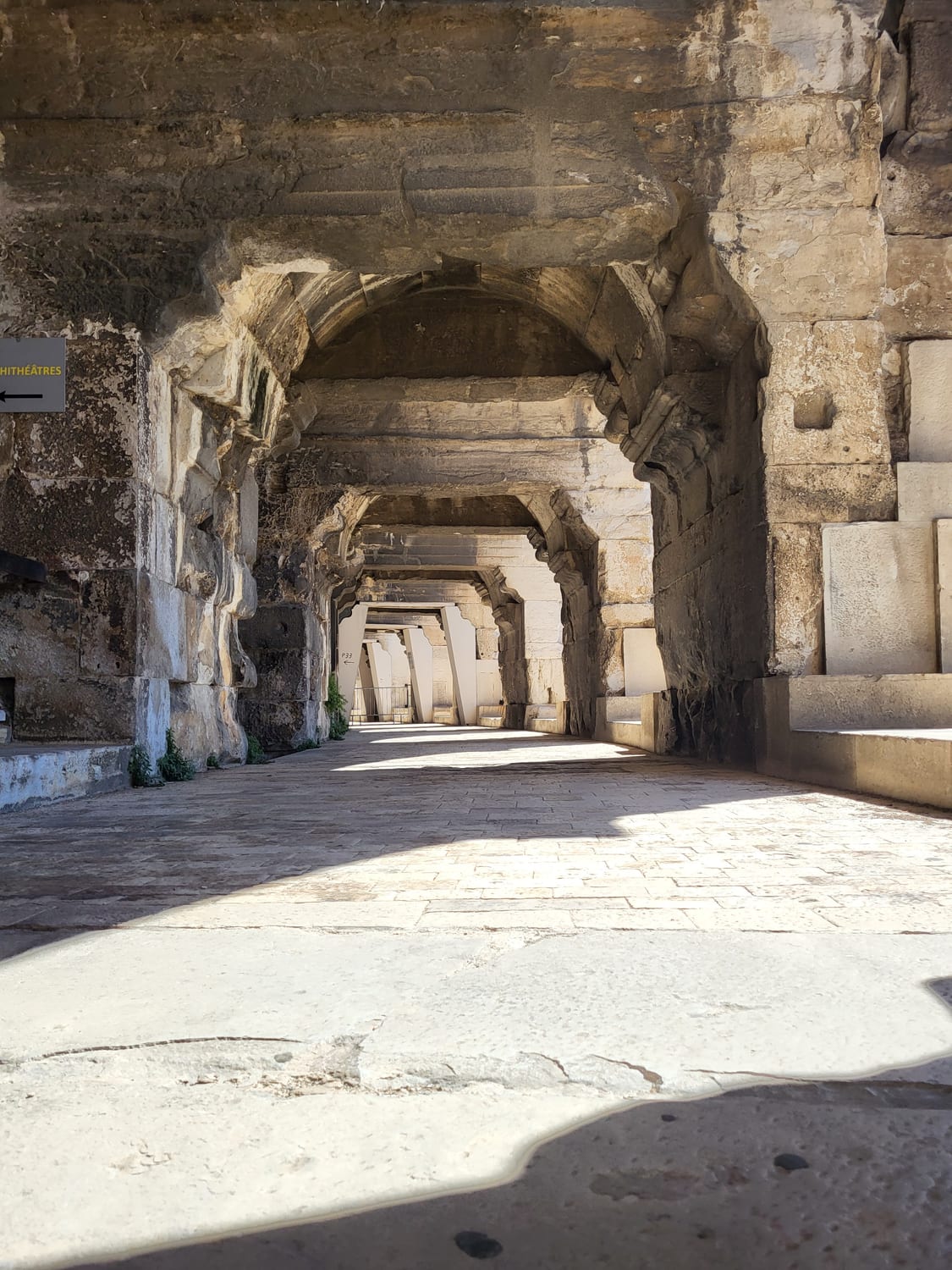 la galería exterior de la planta baja de la Arena de Nimes, con sus pilares, sus bóvedas de piedra y la señalización del anfiteatro
