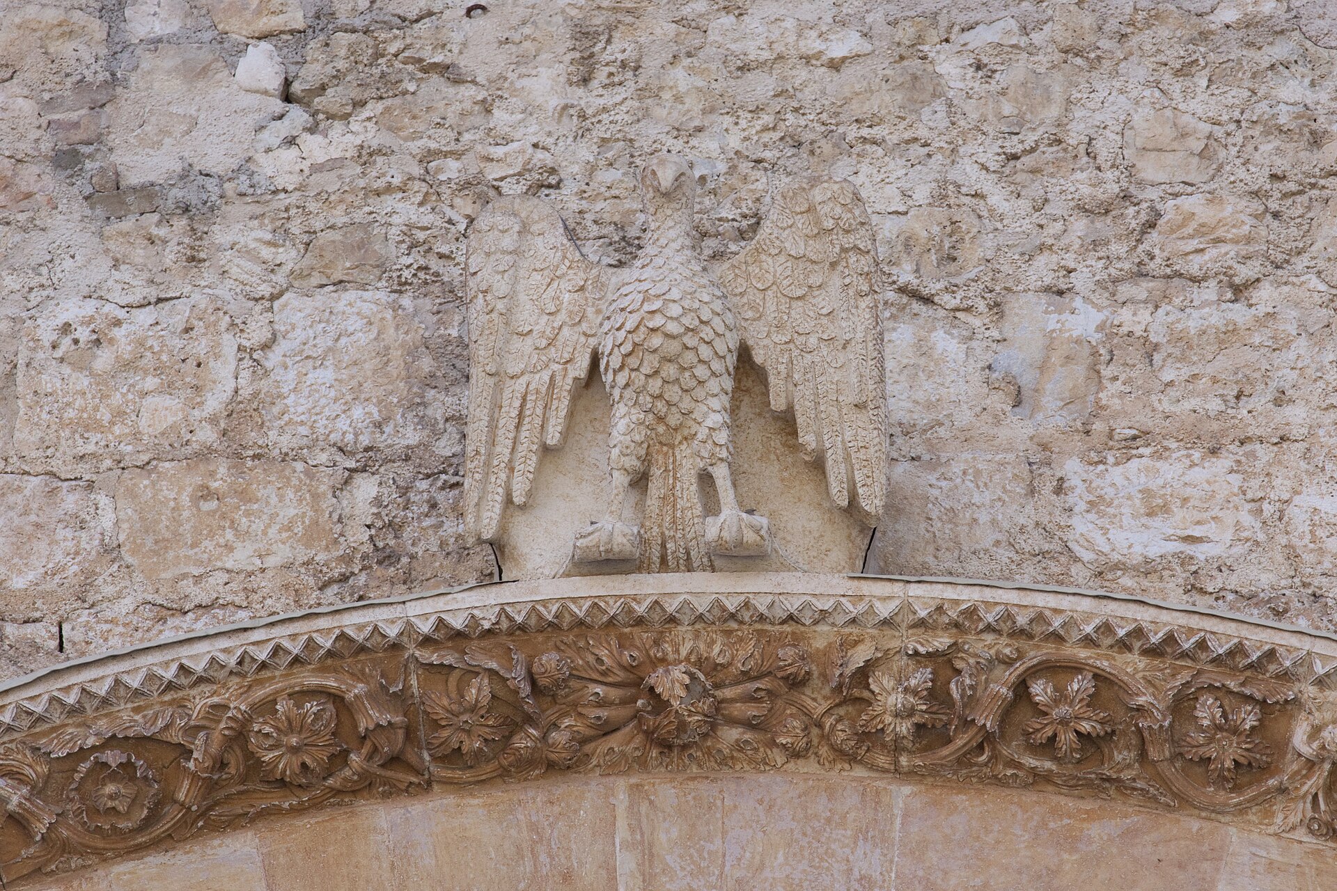un aquila di pietra con le ali aperte scolpita sopra l archivolto di un portale di collemaggio