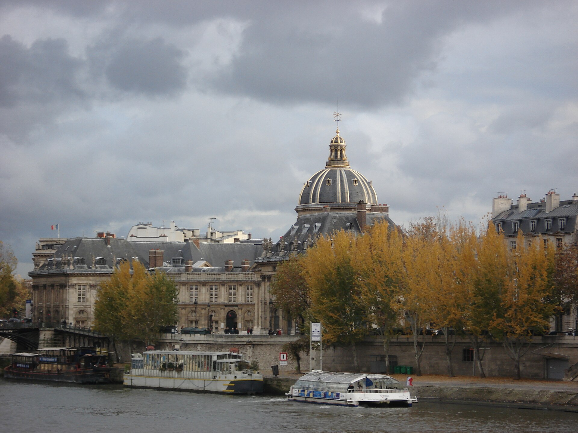 una veduta dalla senna verso la cupola dorata dell’institut de france, con un battello turistico che passa davanti alla riva