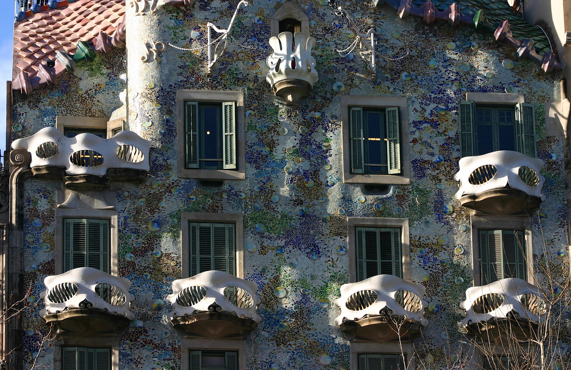 la facciata di casa batllo coperta di cocci colorati, con i balconi bianchi a forma di maschera e il tetto a squame