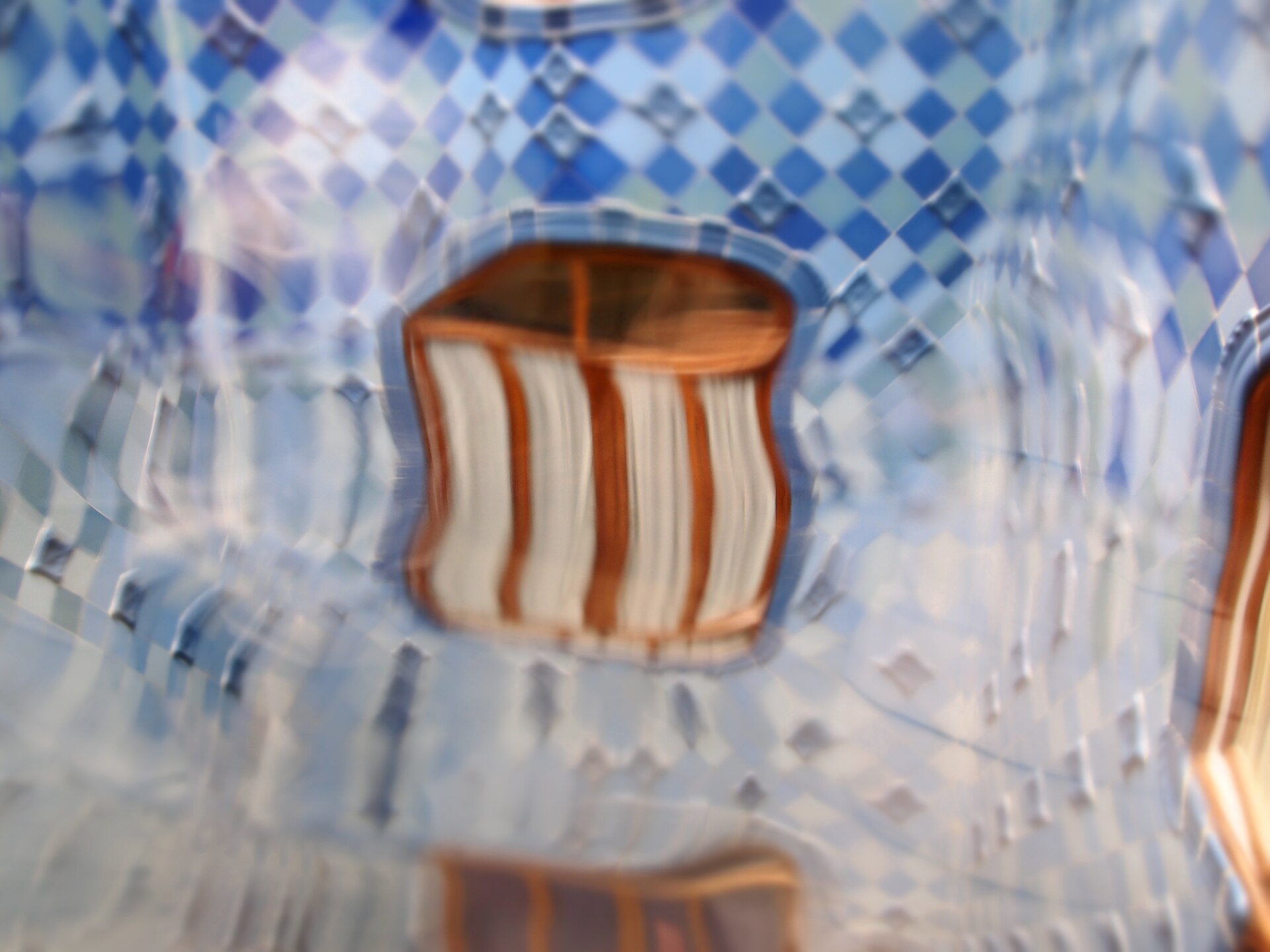 il pozzo di luce di casa batllo visto attraverso un vetro ondulato che deforma le piastrelle blu e una finestra