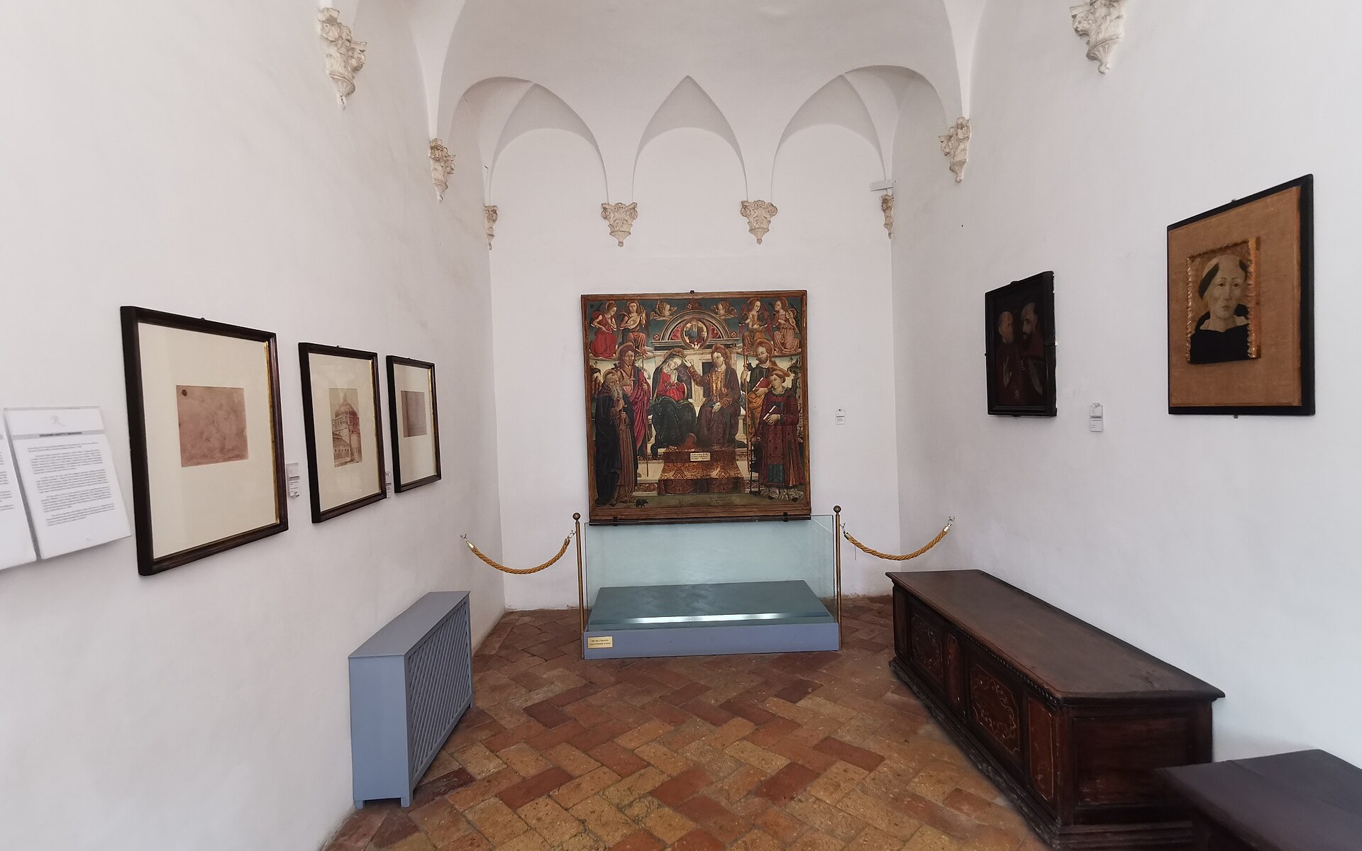 salle intérieure de la maison natale de raphaël à urbino avec des voûtes d’arêtes et des tableaux exposés