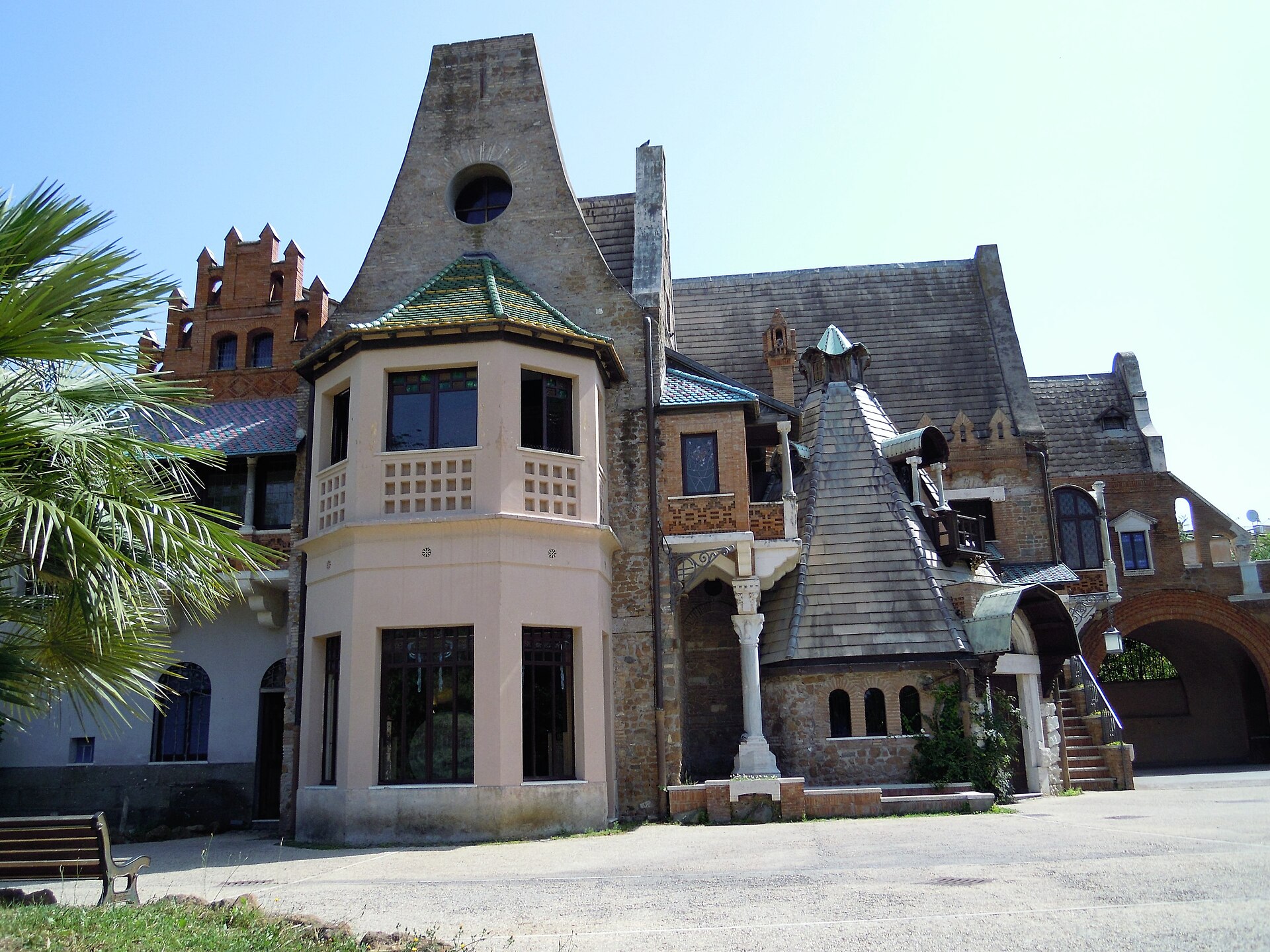 the casina delle civette seen from the forecourt, with the pink bay-window turret under a roof of green majolica, the pointed gable with a round window, a crenellated brick tower on the left and a conical slate roof on the right
