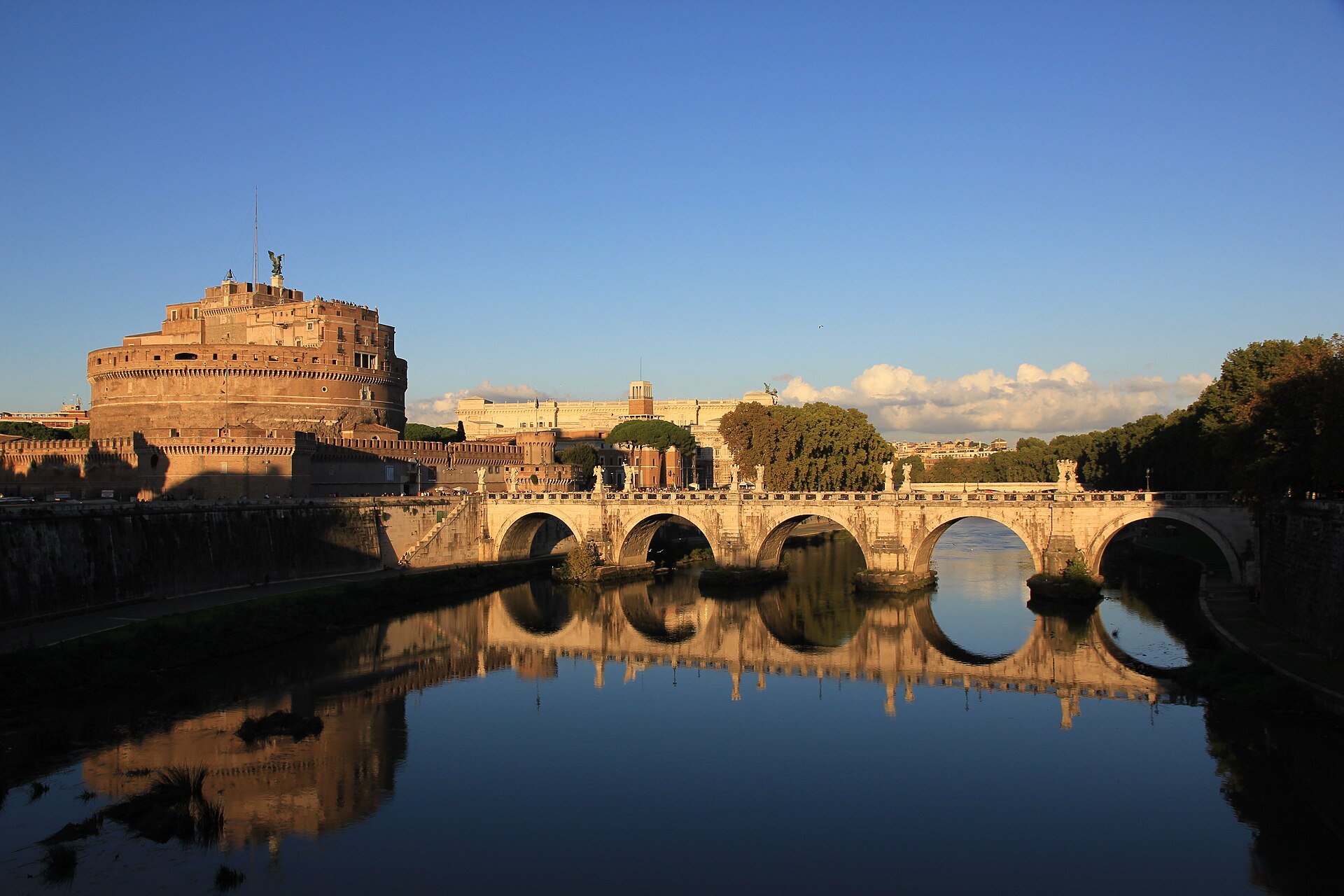 castel sant’angelo a roma visto dal tevere, con il tamburo cilindrico, l’angelo di bronzo in cima e il ponte con le statue riflesso nell’acqua