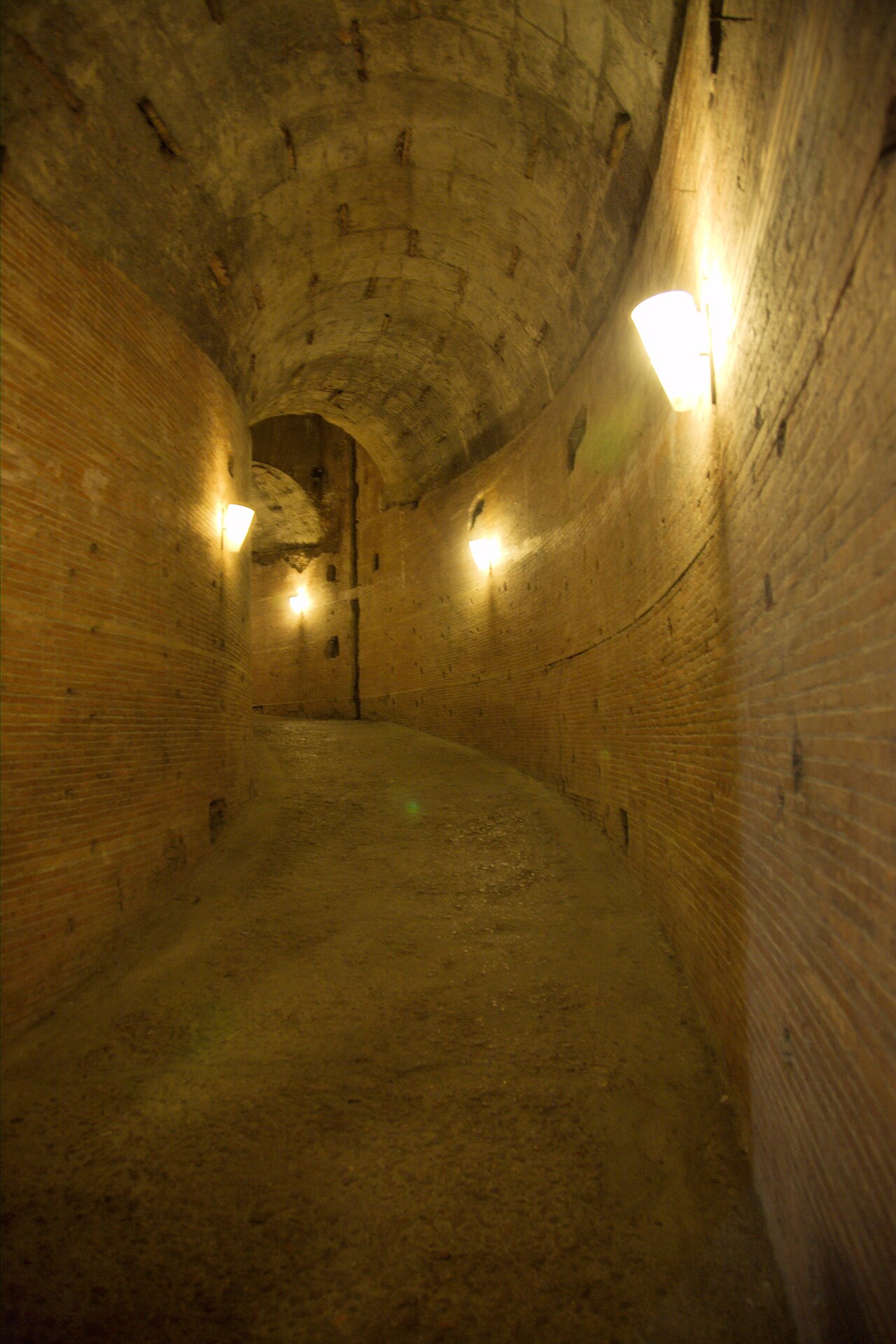 la rampa elicoidale dentro il mausoleo di adriano, con le pareti in mattoni, la volta a botte e il pavimento in terra battuta illuminato dalle lampade