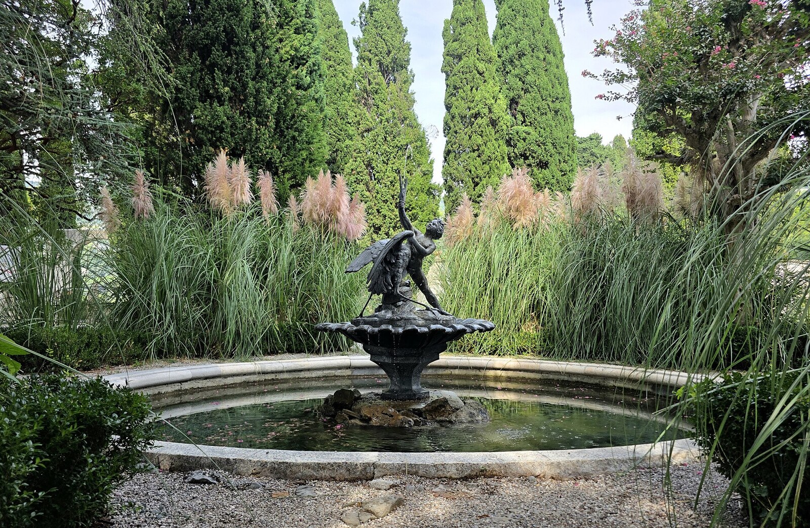 una fontana con statua nel parco di miramare fra i cipressi e i ciuffi di erba della pampa