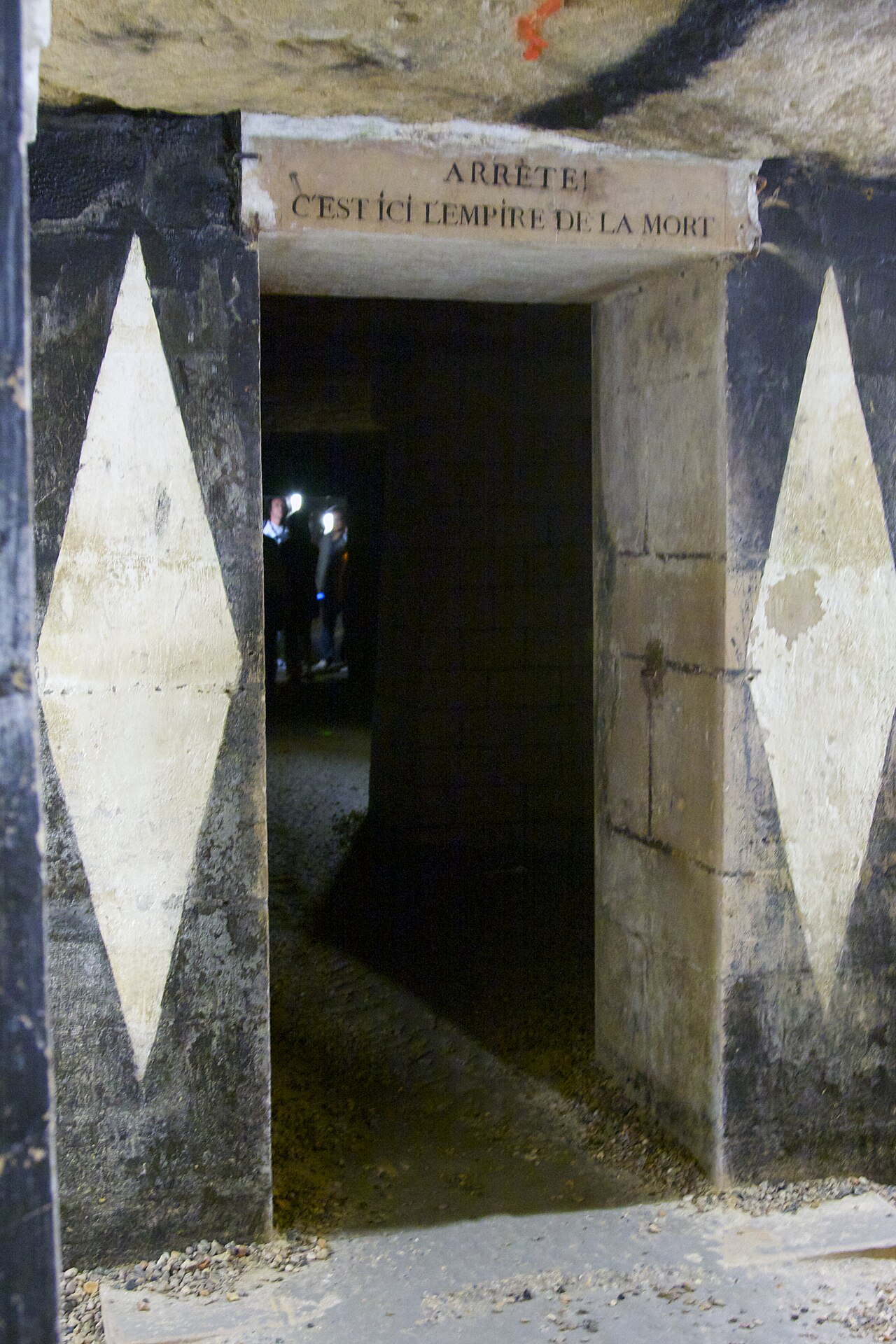 la soglia di pietra che introduce all ossario, con l iscrizione arrete c est ici l empire de la mort sull architrave e gli stipiti dipinti a grandi losanghe bianche e nere, e due visitatori con la torcia nel buio oltre la porta