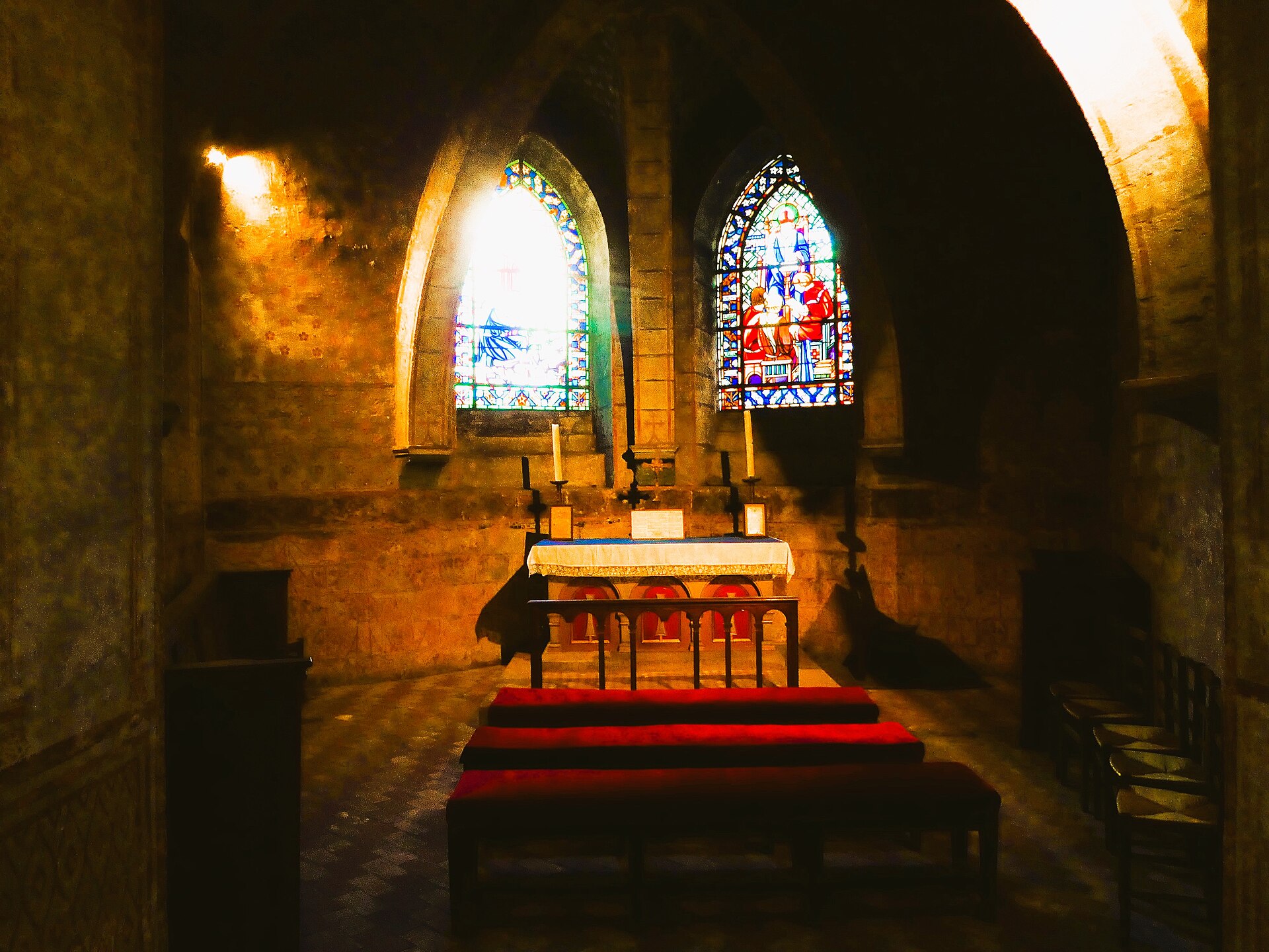 la cappella gotica di saint-fulbert nella cripta di chartres, con le vetrate colorate illuminate, l’altare con le candele accese e le panche rosse in primo piano