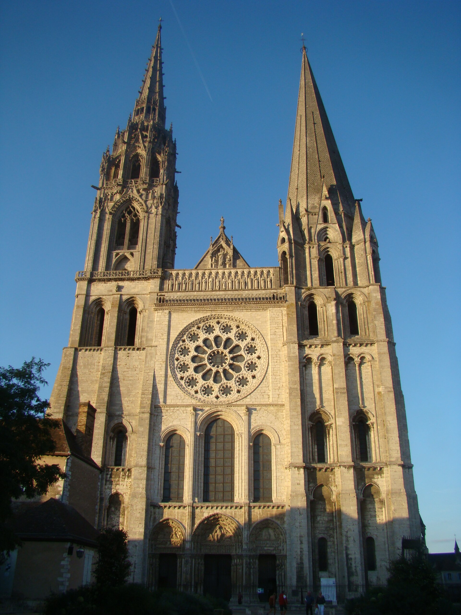 la facciata ovest della cattedrale di chartres al tramonto, con il rosone centrale e le due guglie diverse fra loro, una gotica fiammeggiante e una più antica e sobria