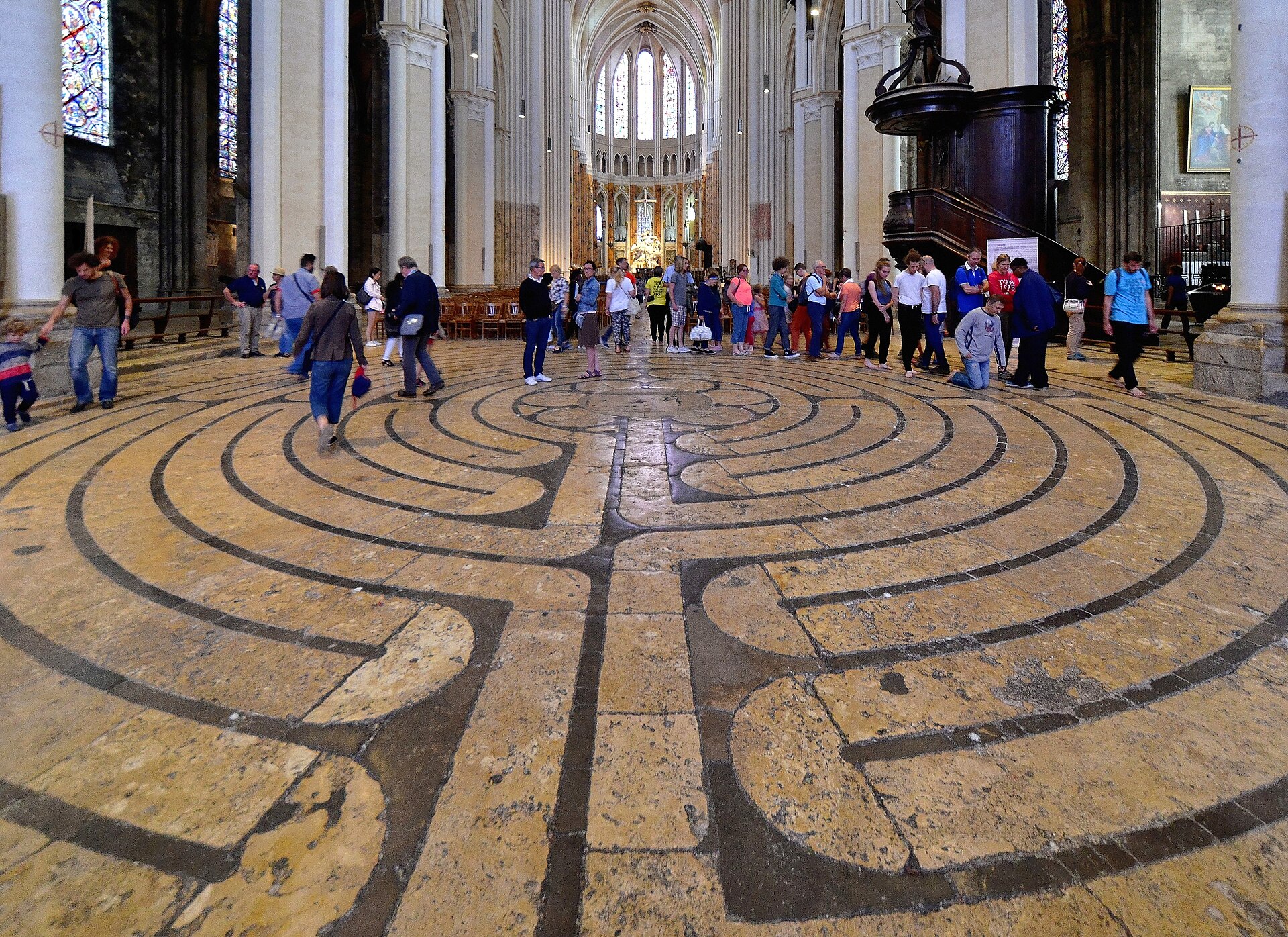il labirinto medievale sul pavimento della navata di chartres, con i visitatori che ne percorrono i giri verso il centro e il coro in fondo oltre le colonne