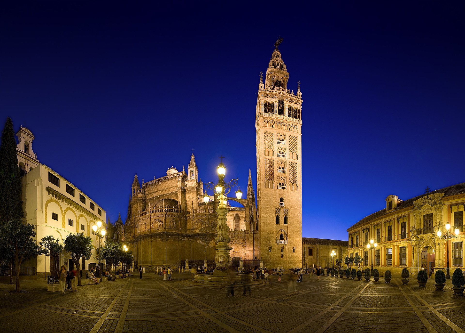 la giralda illuminata nella sera blu sopra plaza virgen de los reyes, con la cattedrale a sinistra e un lampione di ferro in primo piano