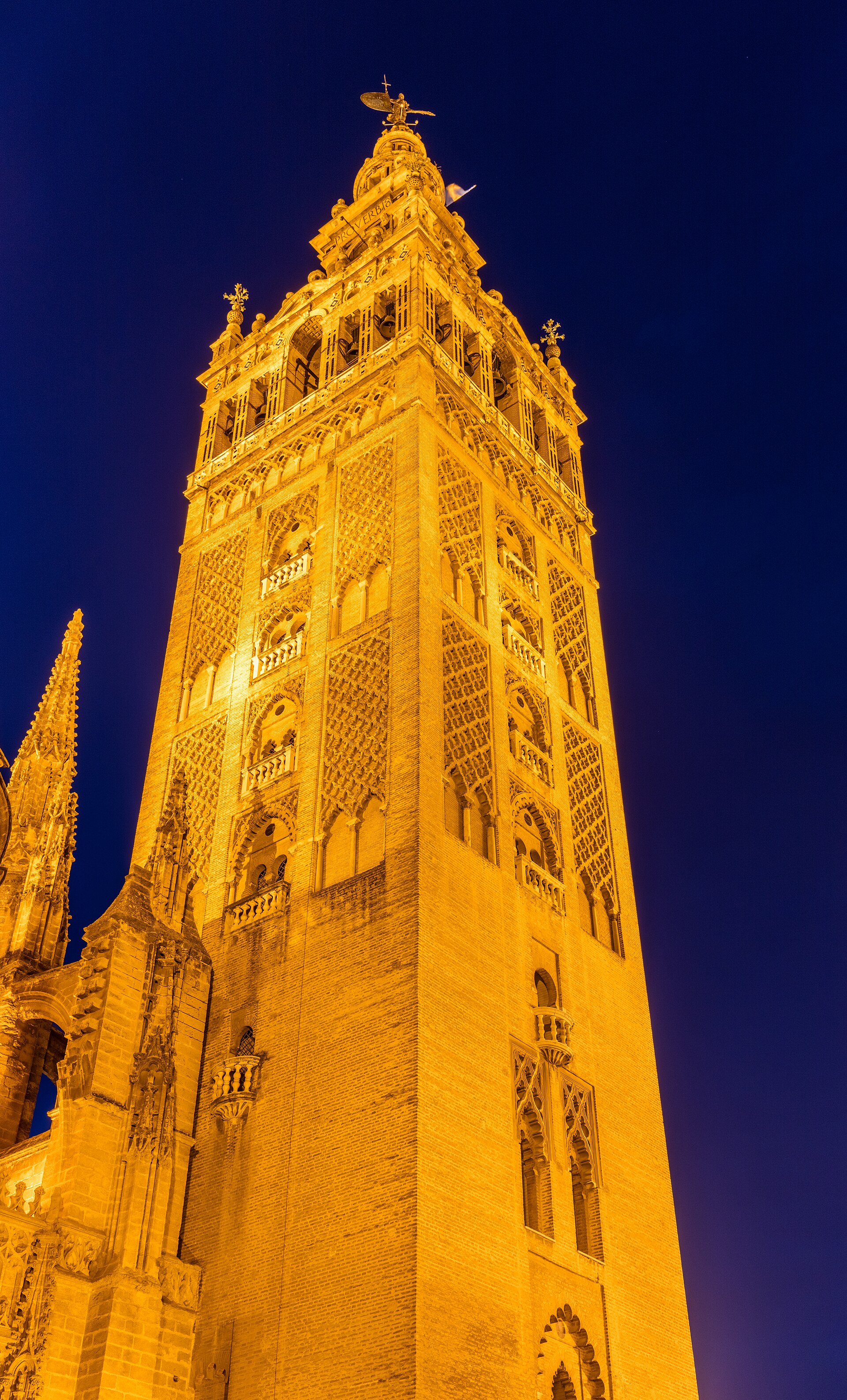 la giralda di notte, illuminata di giallo contro il cielo blu, con la cella delle campane e la statua della fede in cima