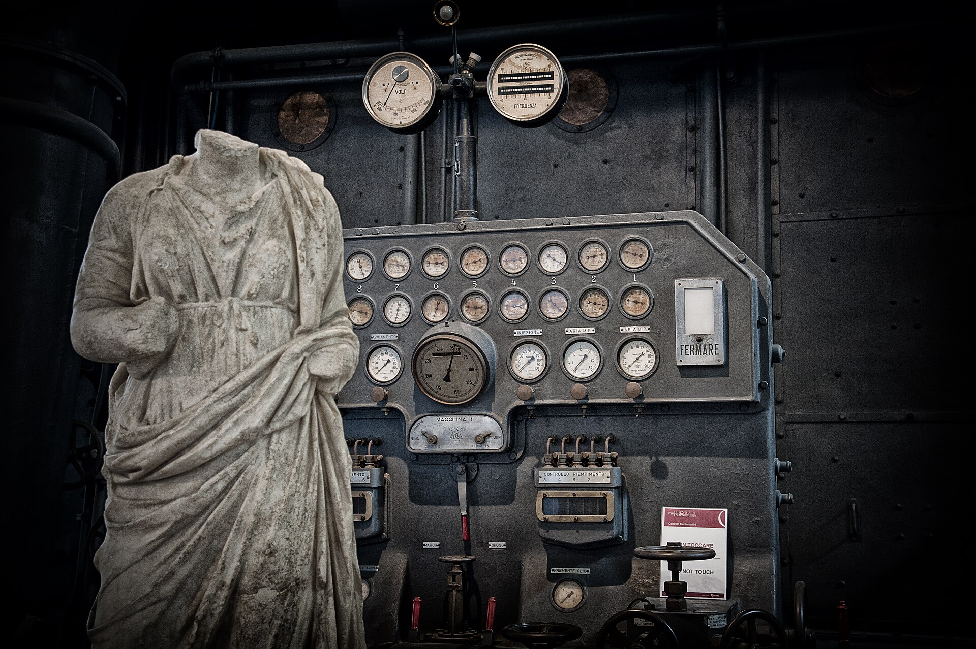statua romana acefala in marmo bianco davanti al quadro comandi della centrale montemartini a roma, con i quadranti e la leva di arresto