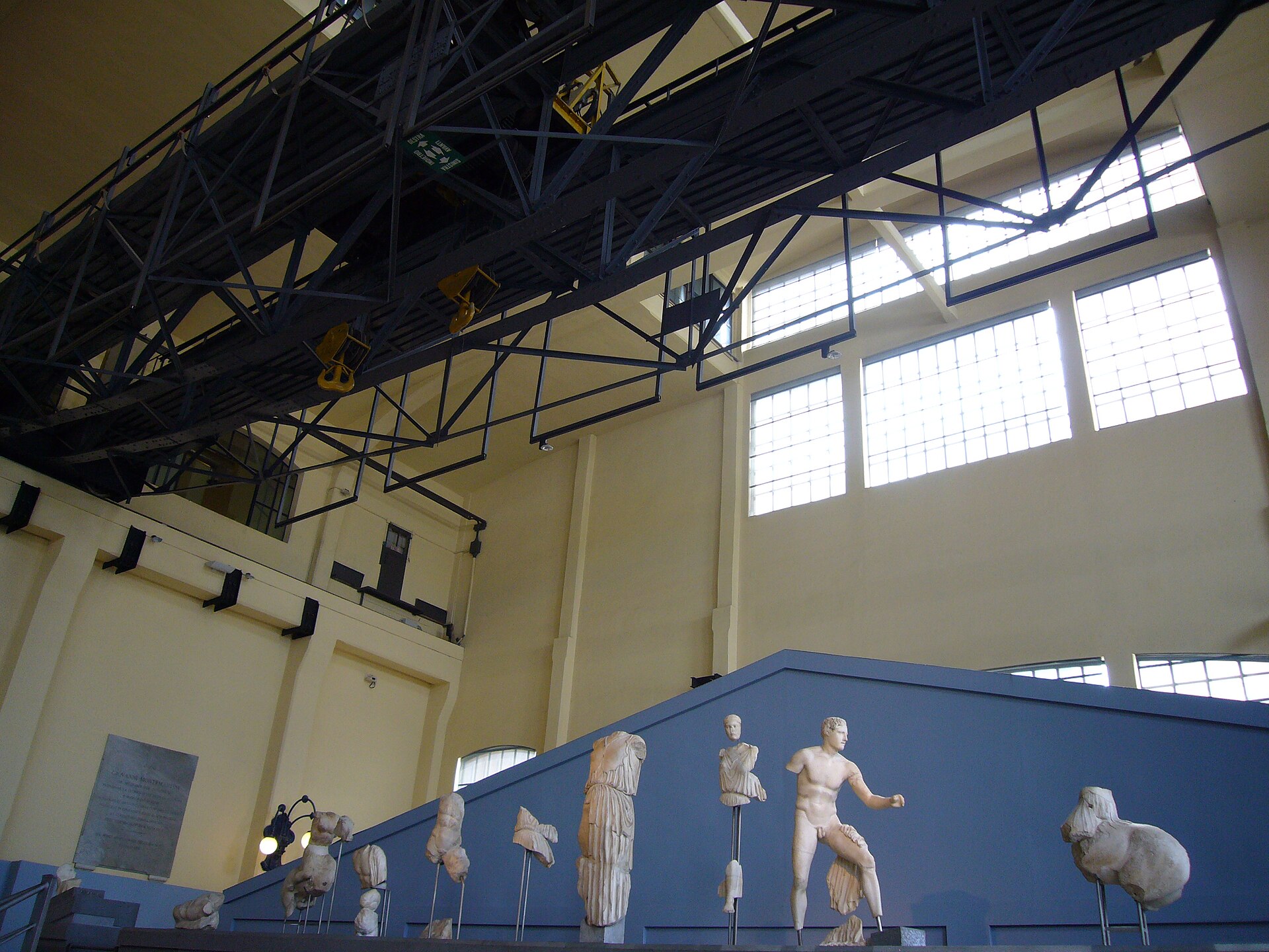 le sculture del frontone del tempio di apollo sosiano rimontate su un podio a gradoni davanti alla parete blu, nella sala macchine della centrale montemartini