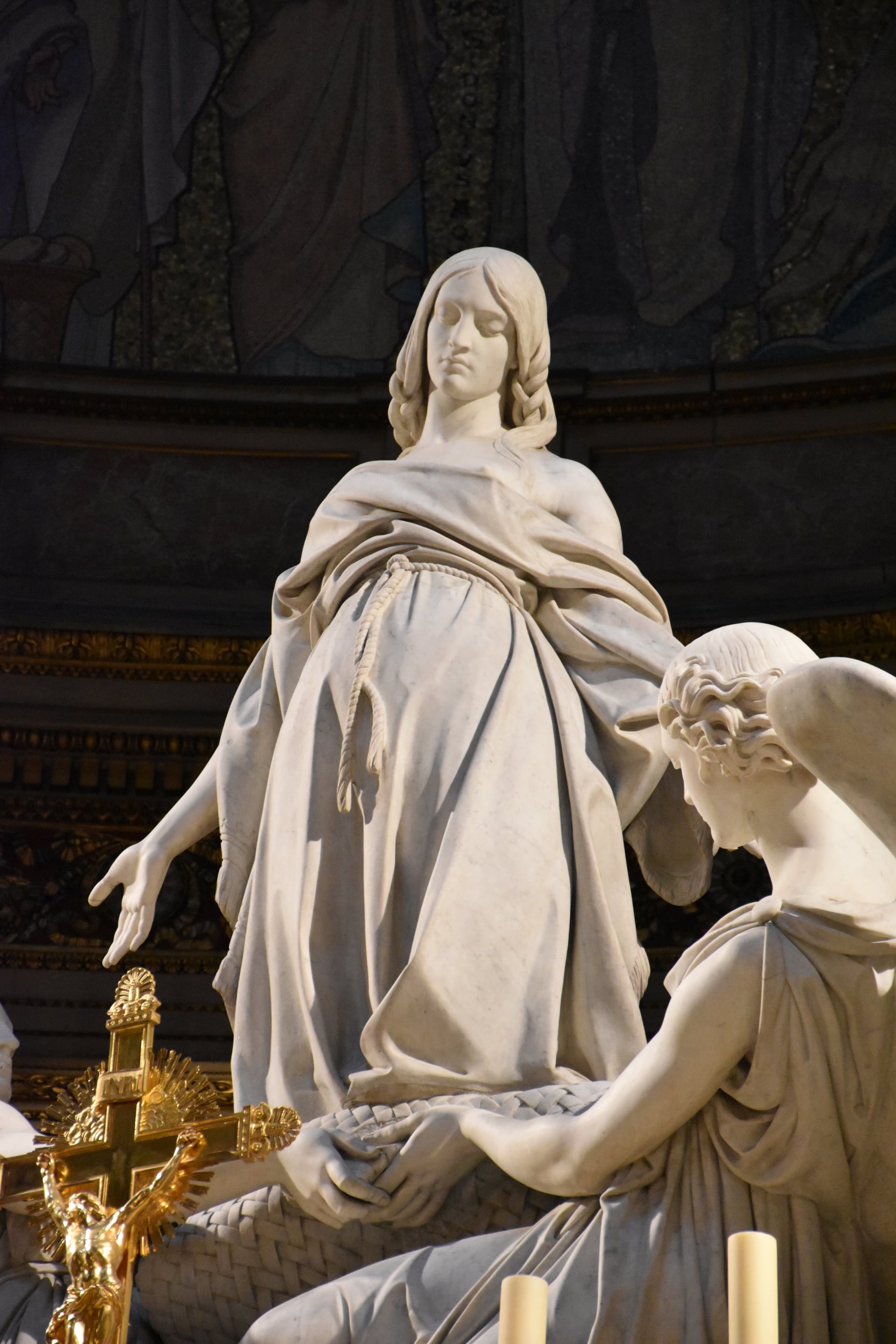 la statua in marmo di maria maddalena sollevata verso l alto, capelli sciolti e cintura a corda, sorretta da un angelo inginocchiato, con una croce processionale dorata in primo piano