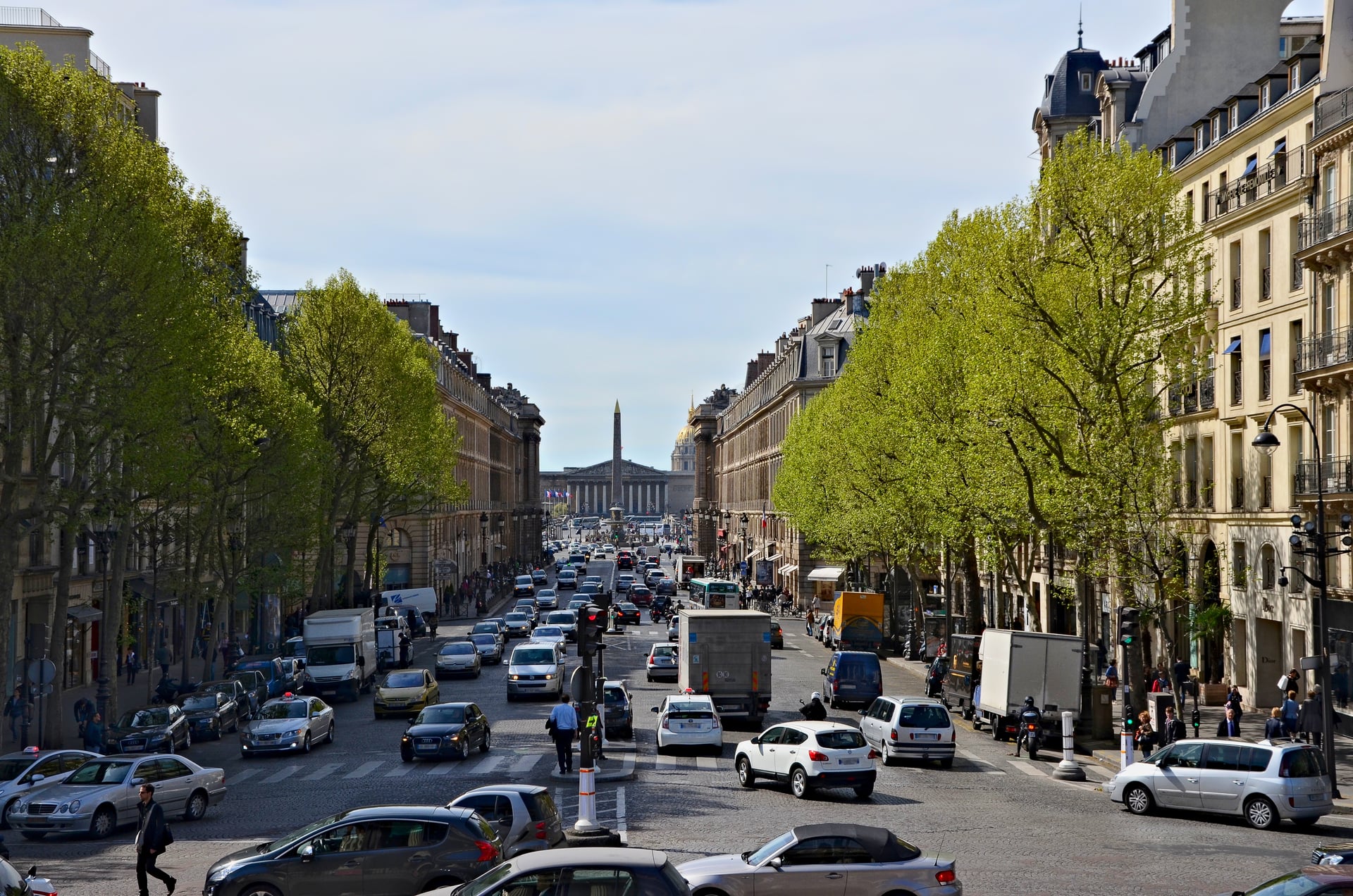 la vista dalla scalinata della madeleine lungo rue royale verso place de la concorde, con l obelisco di luxor e la cupola dorata degli invalides in fondo, traffico e pedoni sulla strada alberata