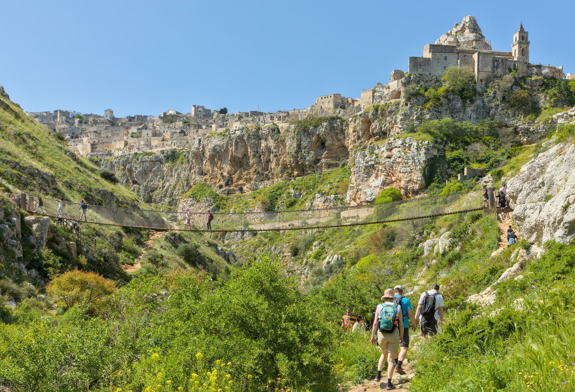 la passerelle suspendue au dessus du torrent gravina avec des randonneurs et les sassi de matera au fond