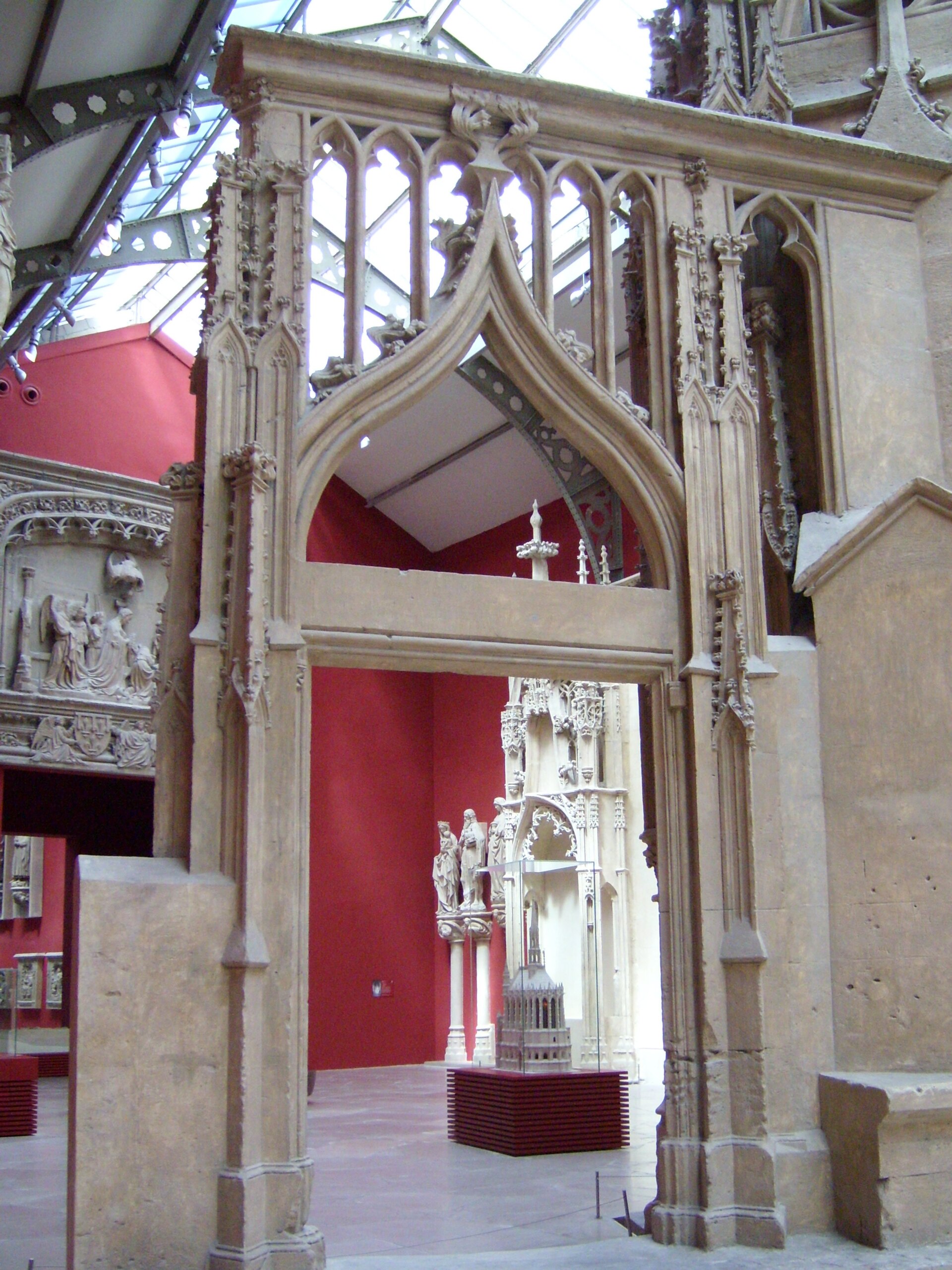 un portale gotico in gesso alla cite de l architecture, con pinnacoli e arcatelle traforate davanti a una parete rossa e il tetto di ferro e vetro del palais de chaillot