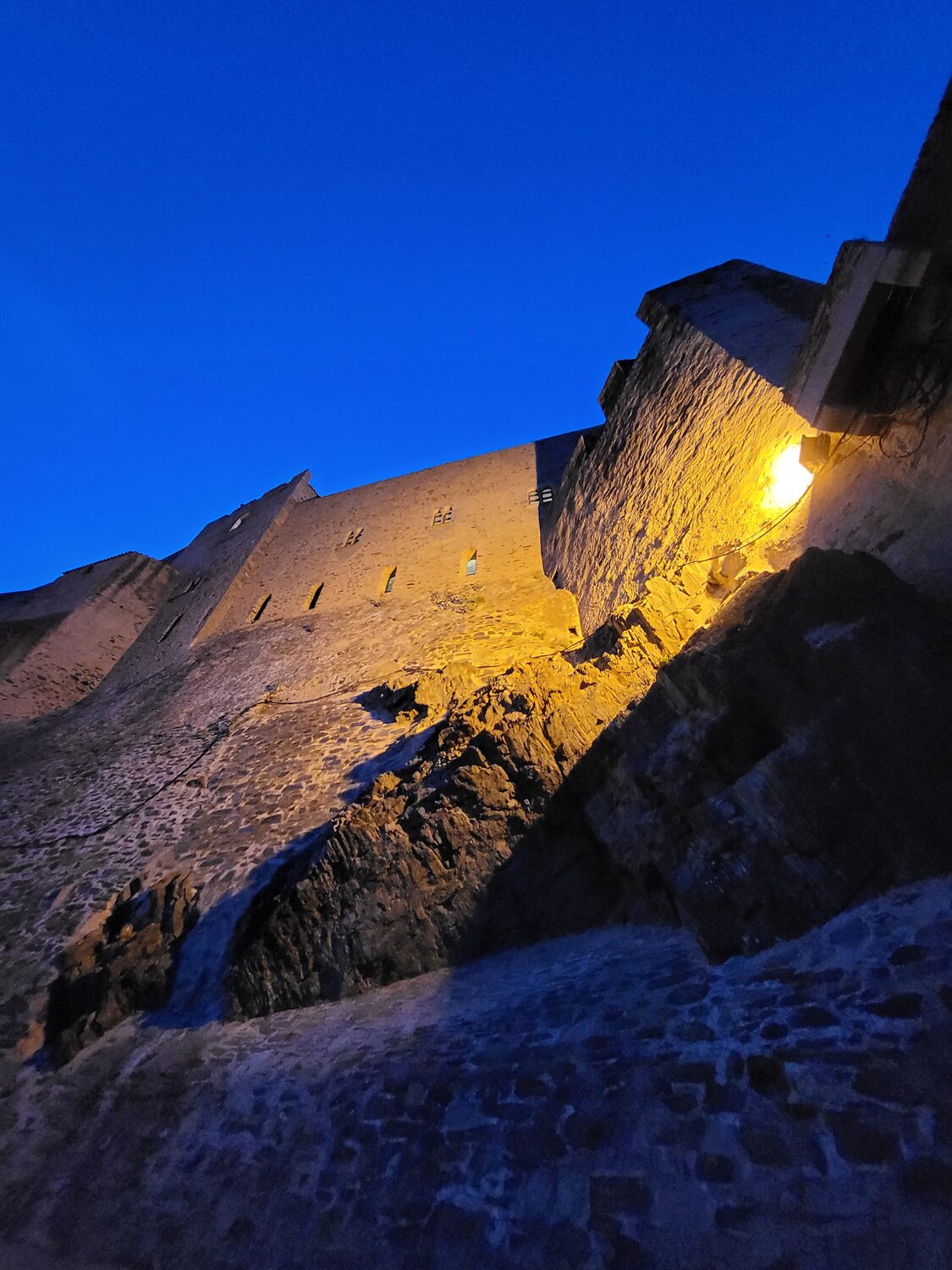 la muraglia del Château Royal di Collioure vista dal basso all’ora blu, illuminata da una lampada