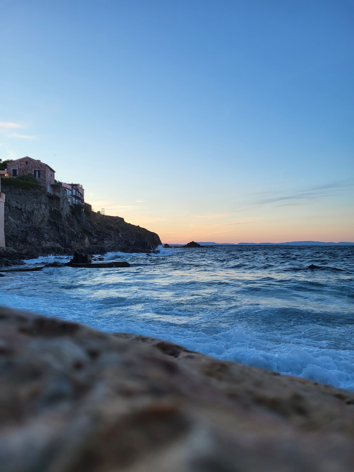 la costa rocciosa di Collioure al tramonto, con il mare mosso e le montagne all’orizzonte