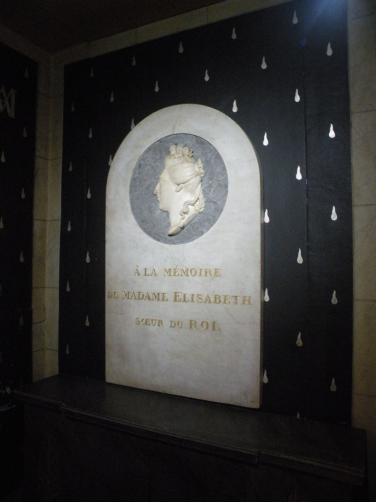 dentro la cappella, una stele di marmo bianco con il profilo scolpito di una donna dentro un tondo di marmo grigio e la scritta dorata a la memoire de madame elisabeth soeur du roi, addossata a una parete nera coperta di lacrime bianche