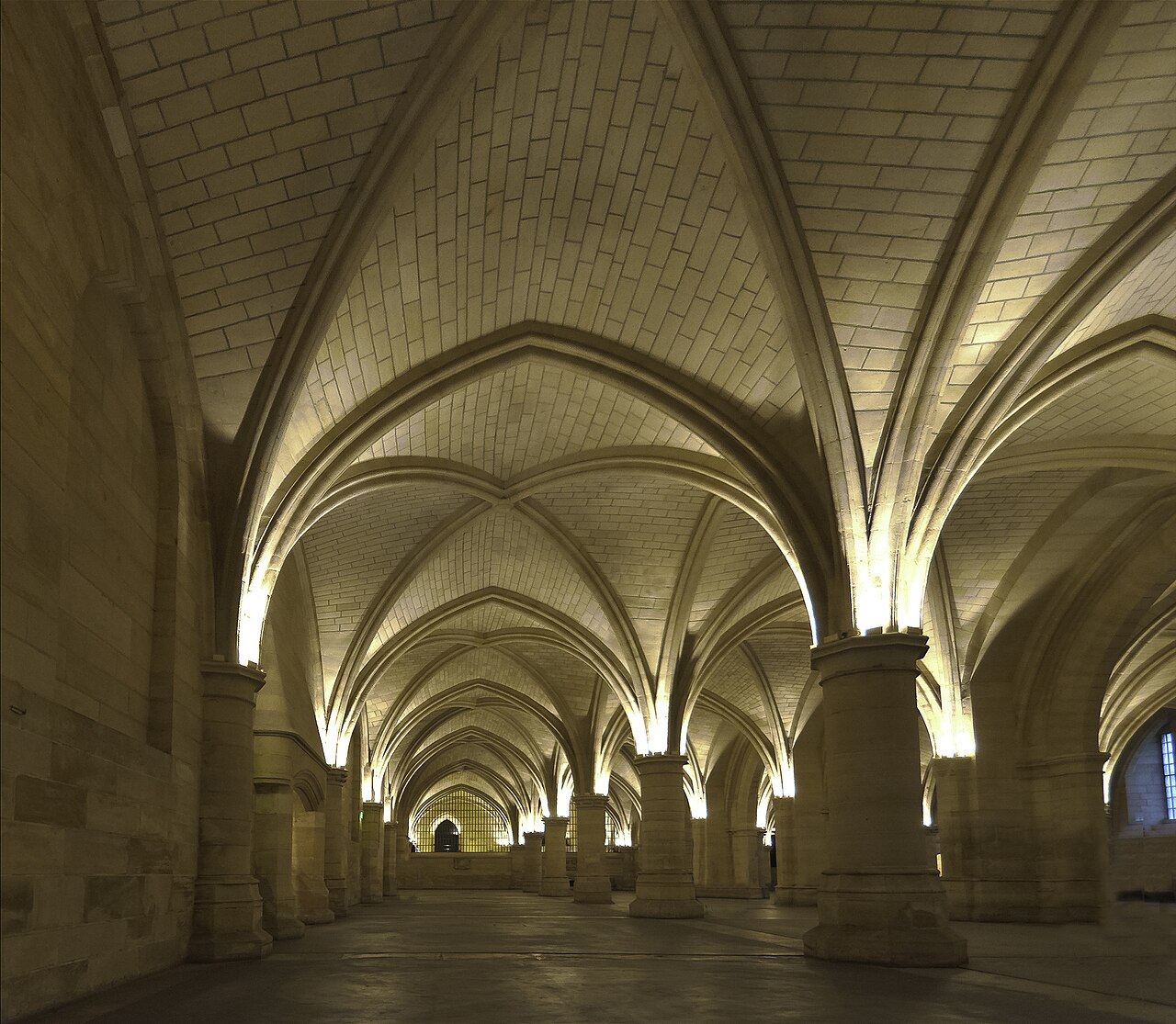 la sala dei gens d armes con le volte a crociera costolonate che poggiano su tozze colonne rotonde, illuminate dal basso da faretti alla base dei capitelli, e le campate che si ripetono in profondita fino a una grata in fondo