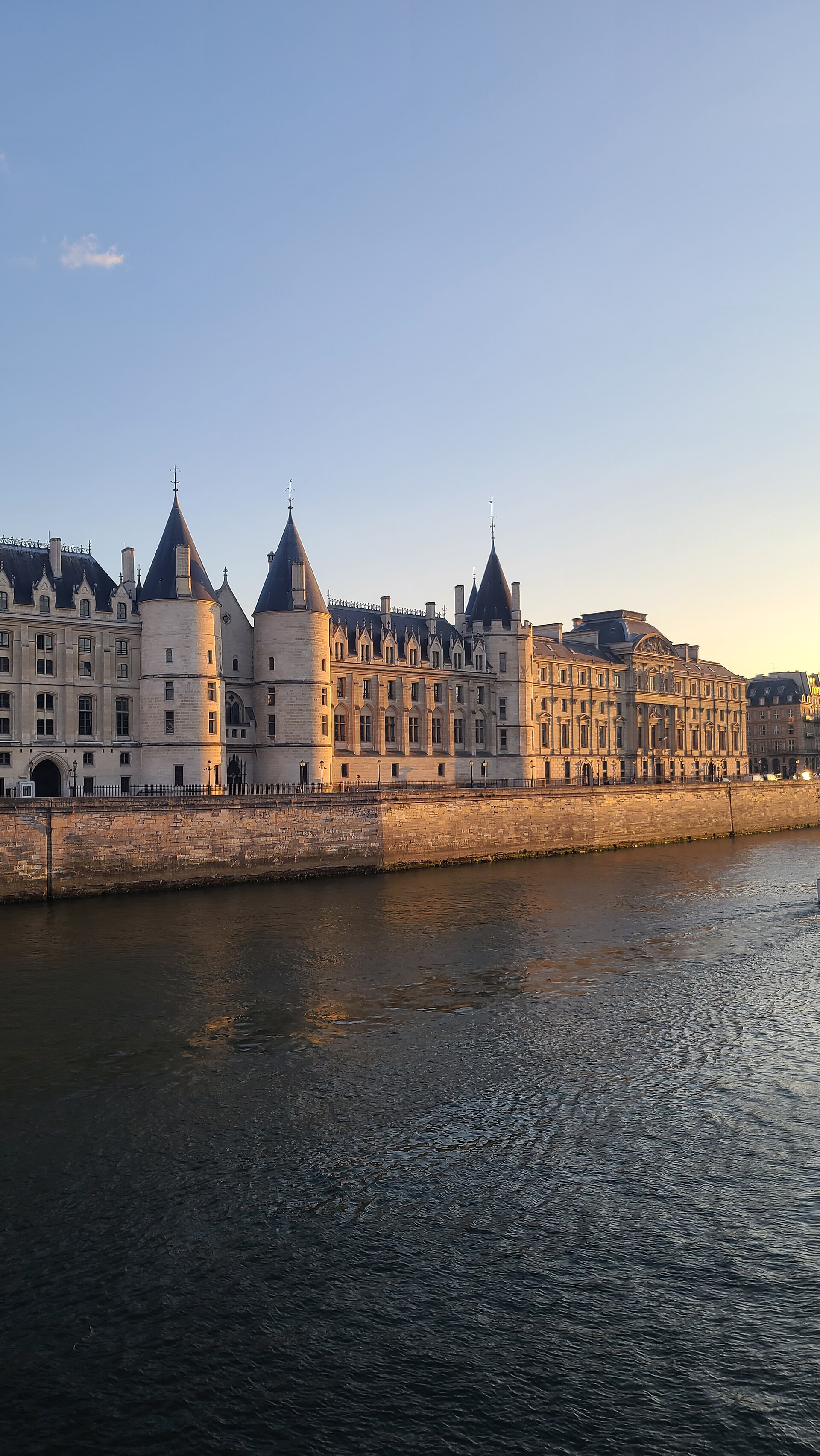 la conciergerie vista dall altra riva della senna nella luce dorata del tramonto, con le torri rotonde dai tetti a cono di ardesia, la lunga facciata sul quai de l horloge e il fiume in primo piano