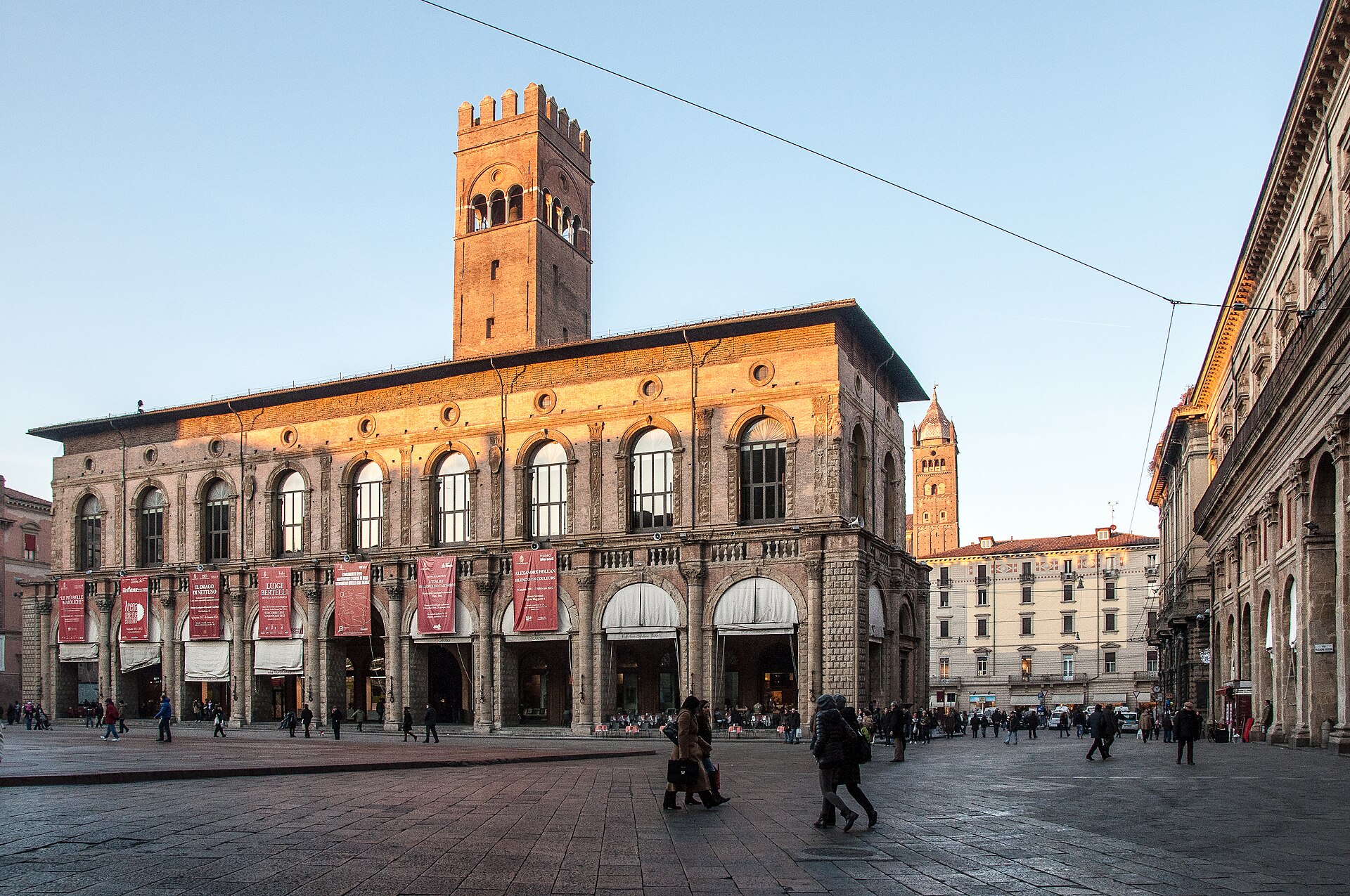 piazza maggiore a bologna con il palazzo del podesta e la torre dell arengo illuminati dal sole basso e i portici in ombra
