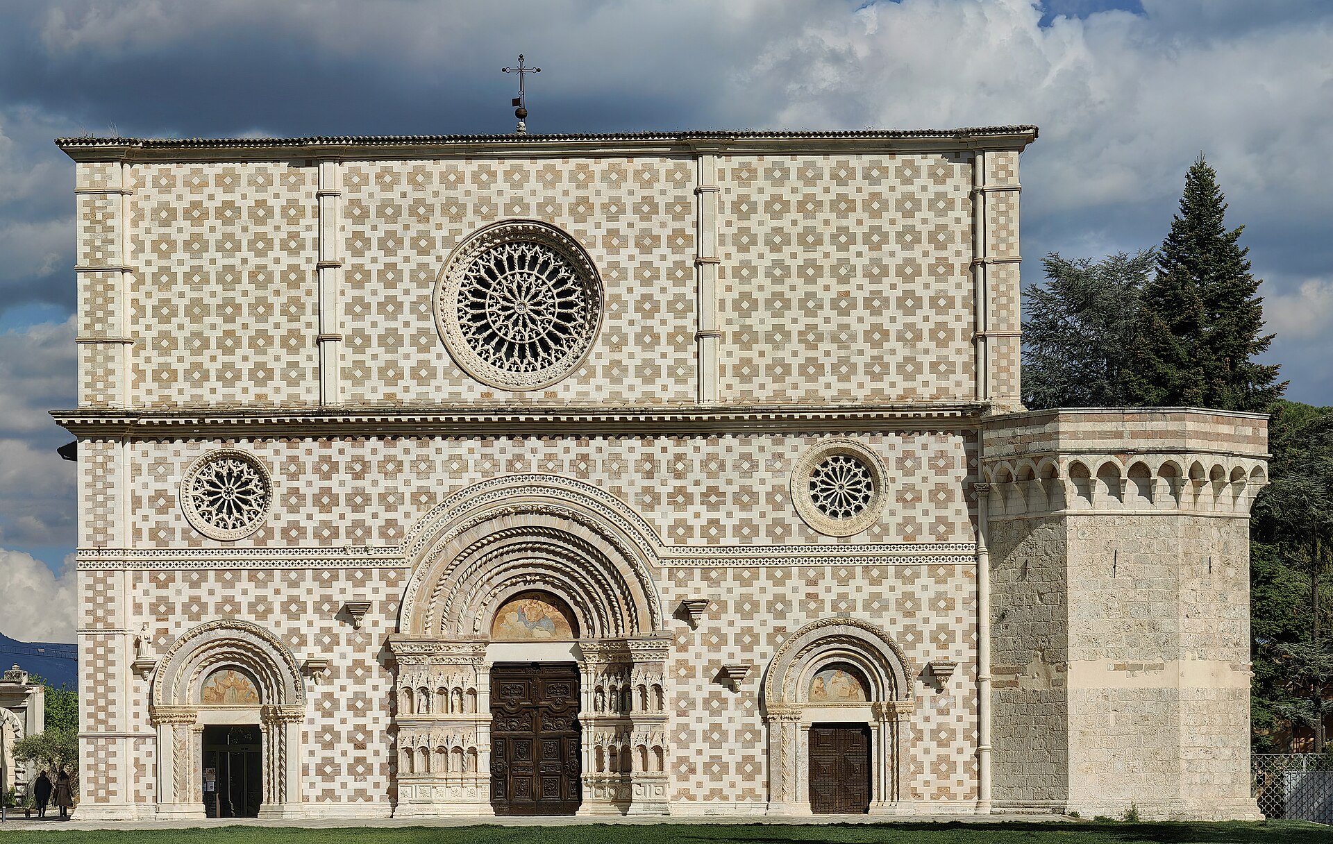 la facciata a scacchi bianchi e rosa della basilica di santa maria di collemaggio con tre rosoni e tre portali