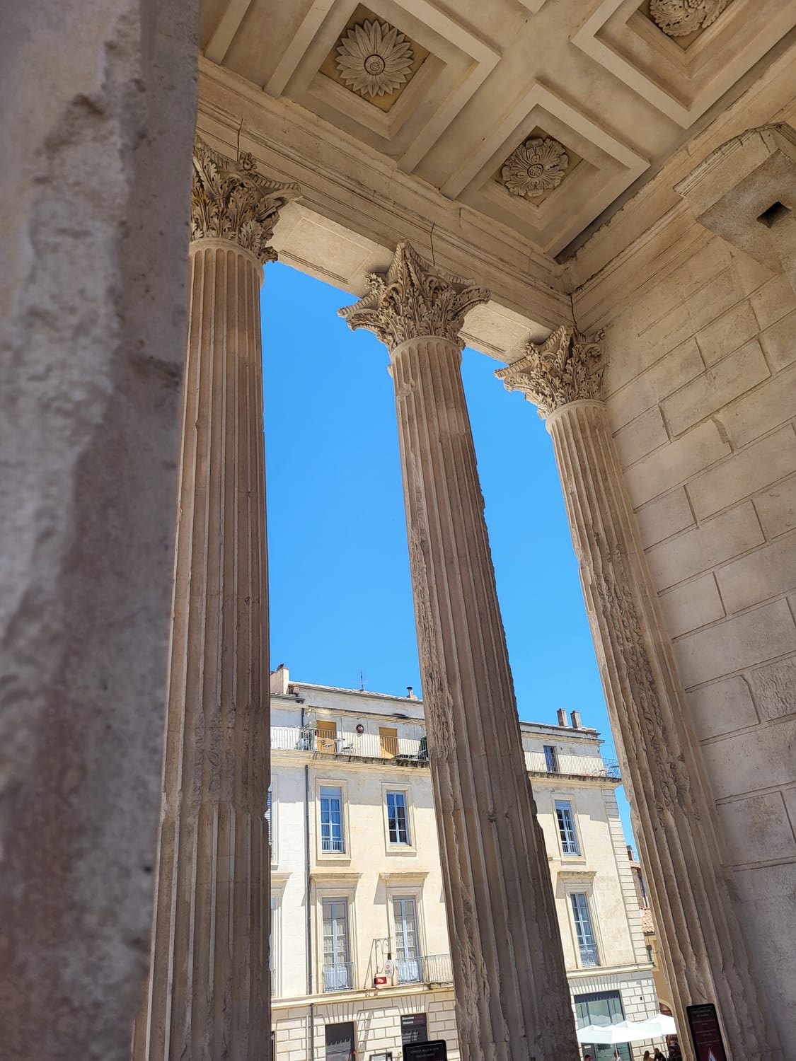 las columnas del pórtico de la Maison Carrée de Nimes enmarcando la plaza y la pared de vidrio del Carré d’Art