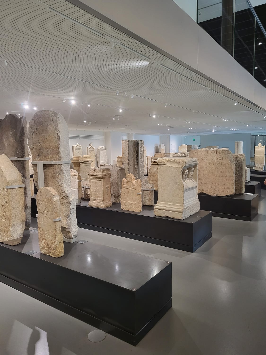 la sala del lapidario en el Musée de la Romanité de Nimes, con estelas e inscripciones funerarias romanas sobre basamentos oscuros