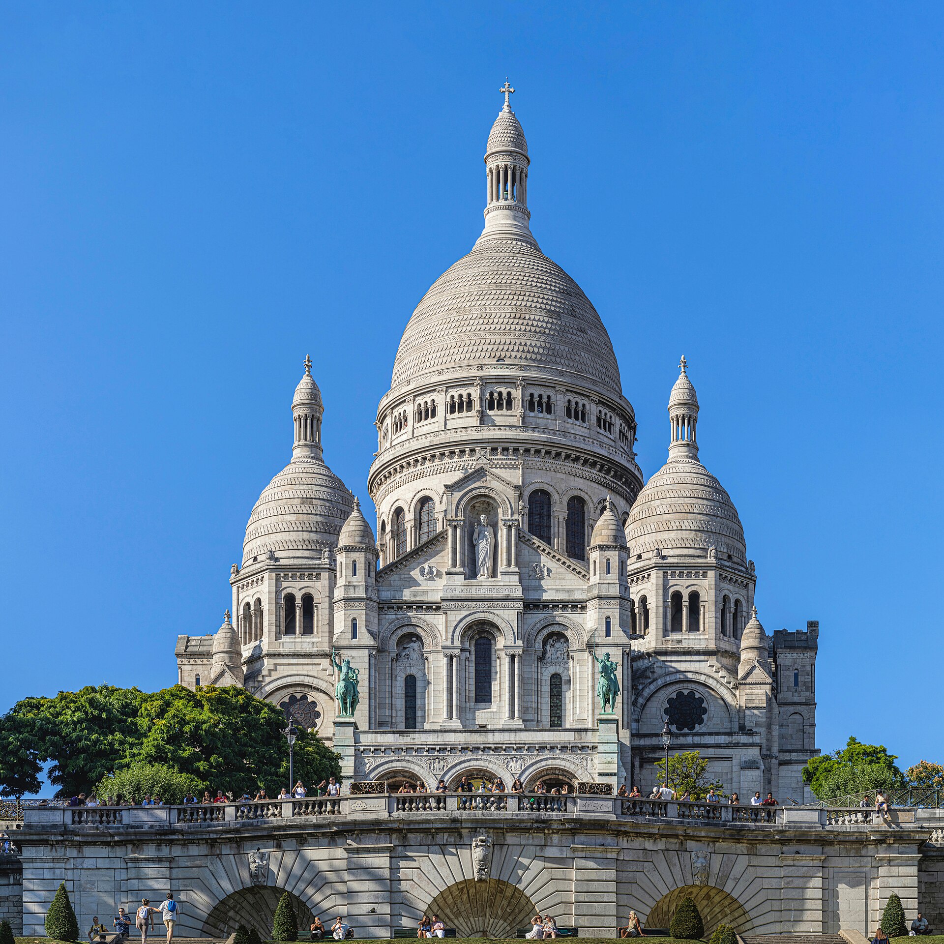 la facciata della basilica del sacro cuore di montmartre vista dal basso, con la cupola bianca centrale, le torrette laterali e le statue equestri di bronzo sulla balaustra