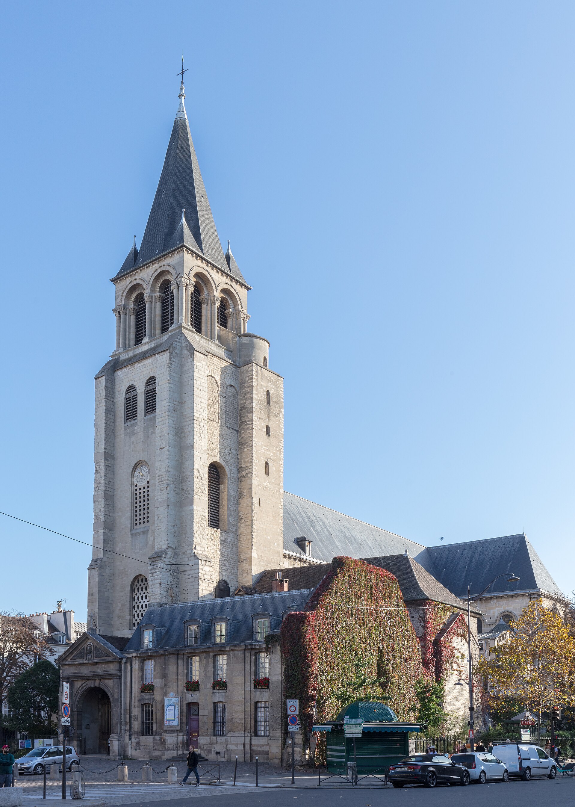 la torre campanaria romanica di saint germain des pres a parigi, con le bifore a colonnine sotto il tetto d ardesia, il fianco della chiesa coperto di edera rossa e le auto parcheggiate lungo la strada