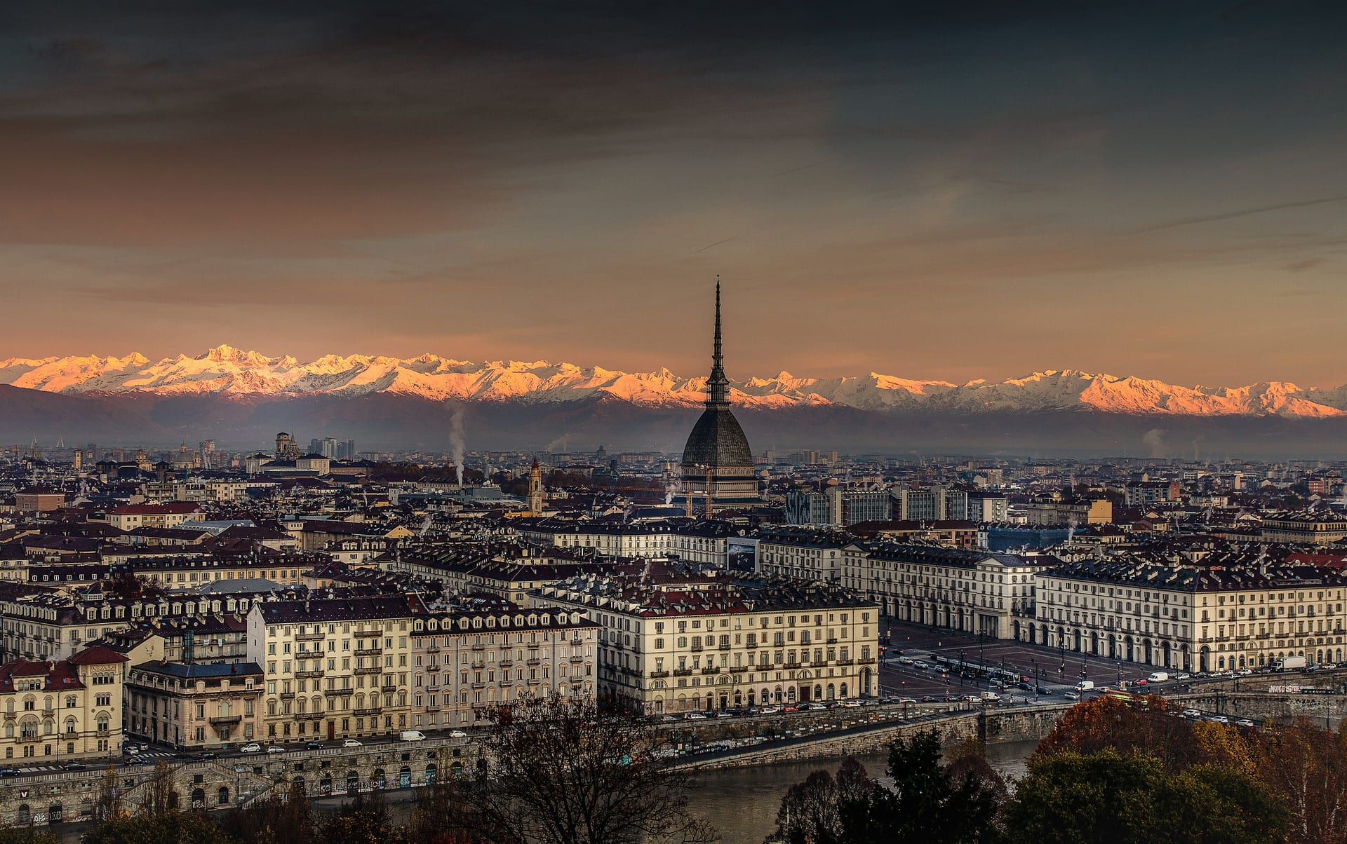 turin at dawn seen from the hill, with the mole antonelliana and the snow covered alps lit pink behind the rooftops