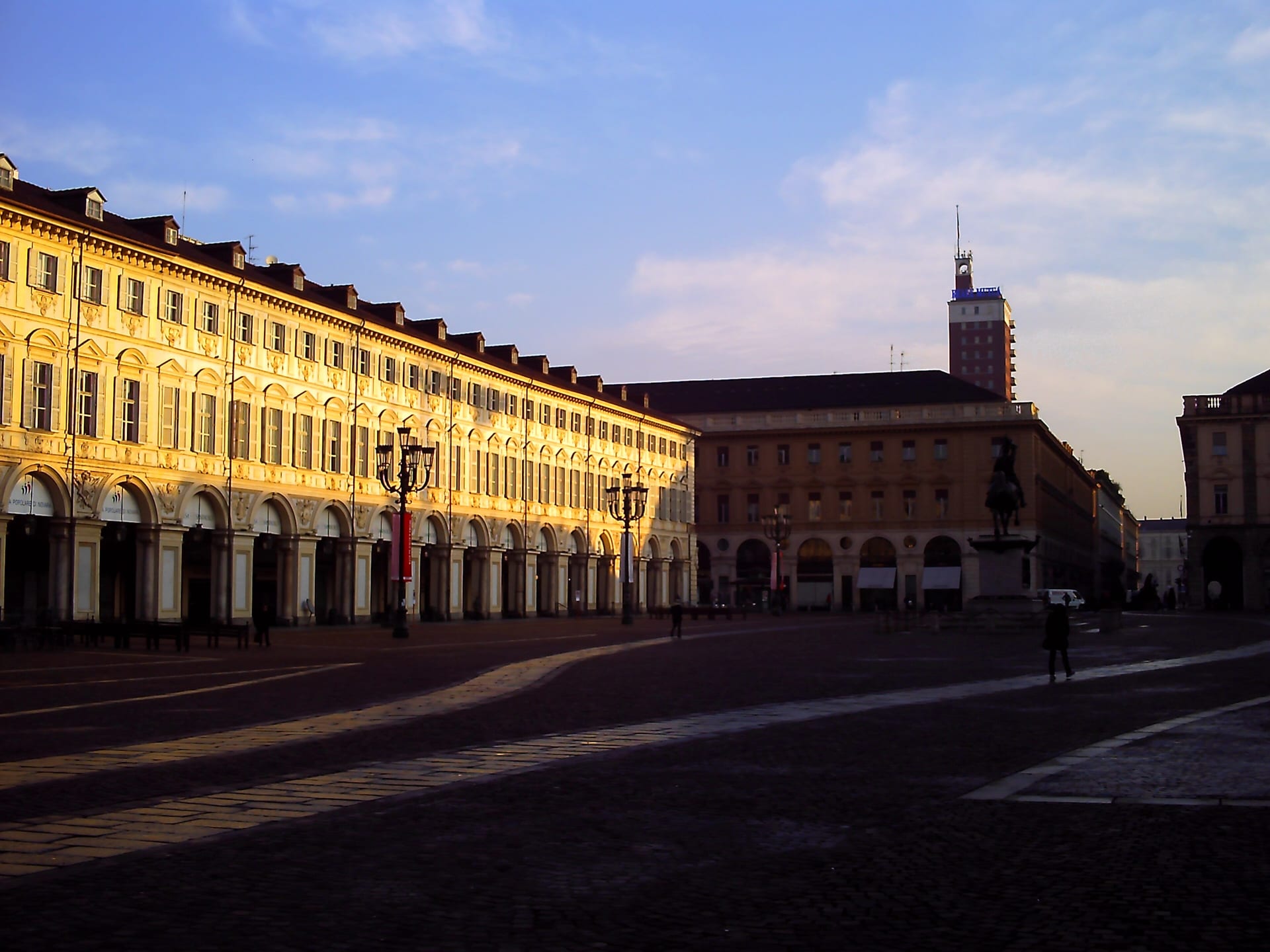 the arcades of piazza san carlo in turin lit by low morning sun, with the torre littoria in the background
