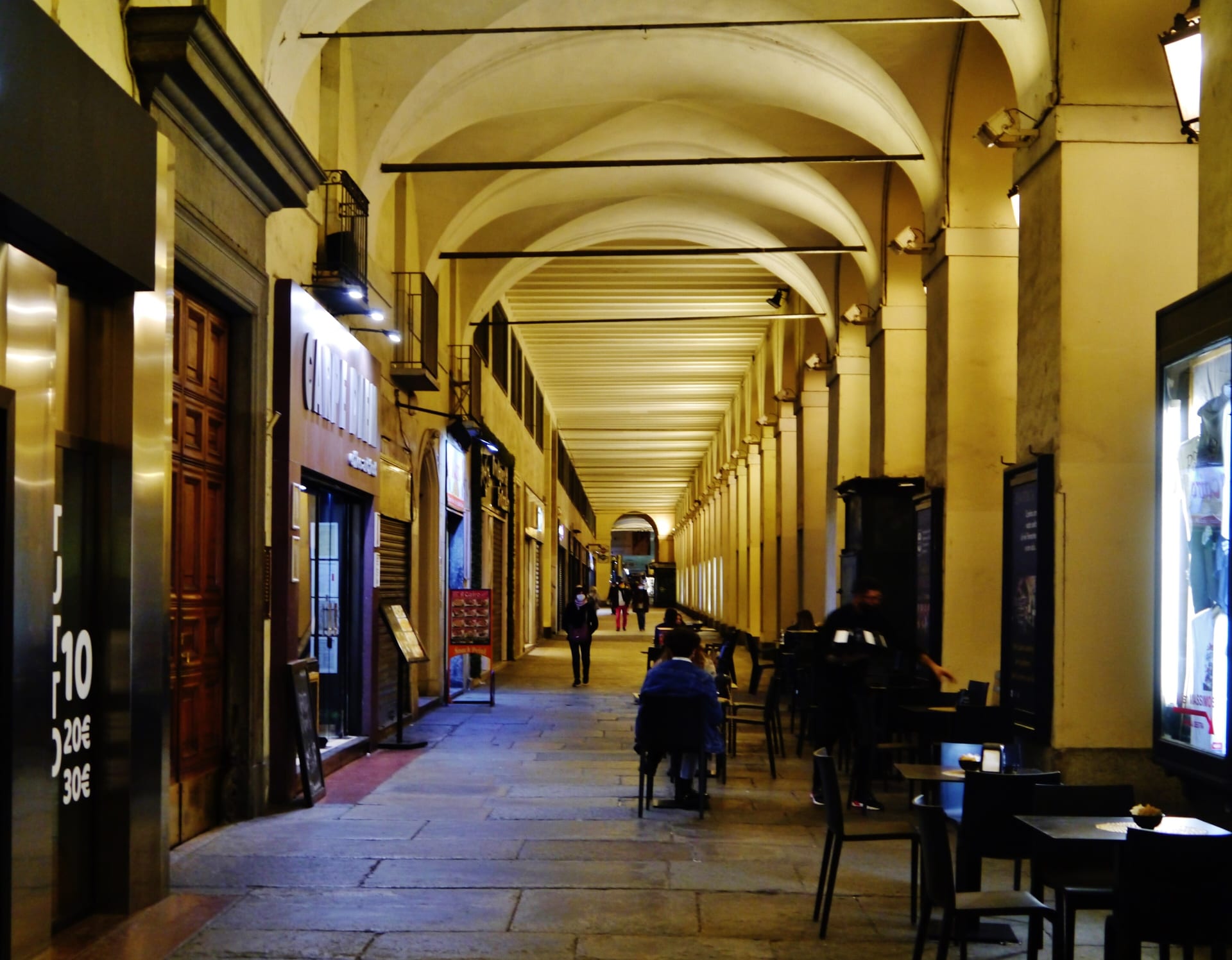 the arcades of via po in turin in the evening, with lit vaults and cafe tables under the arches