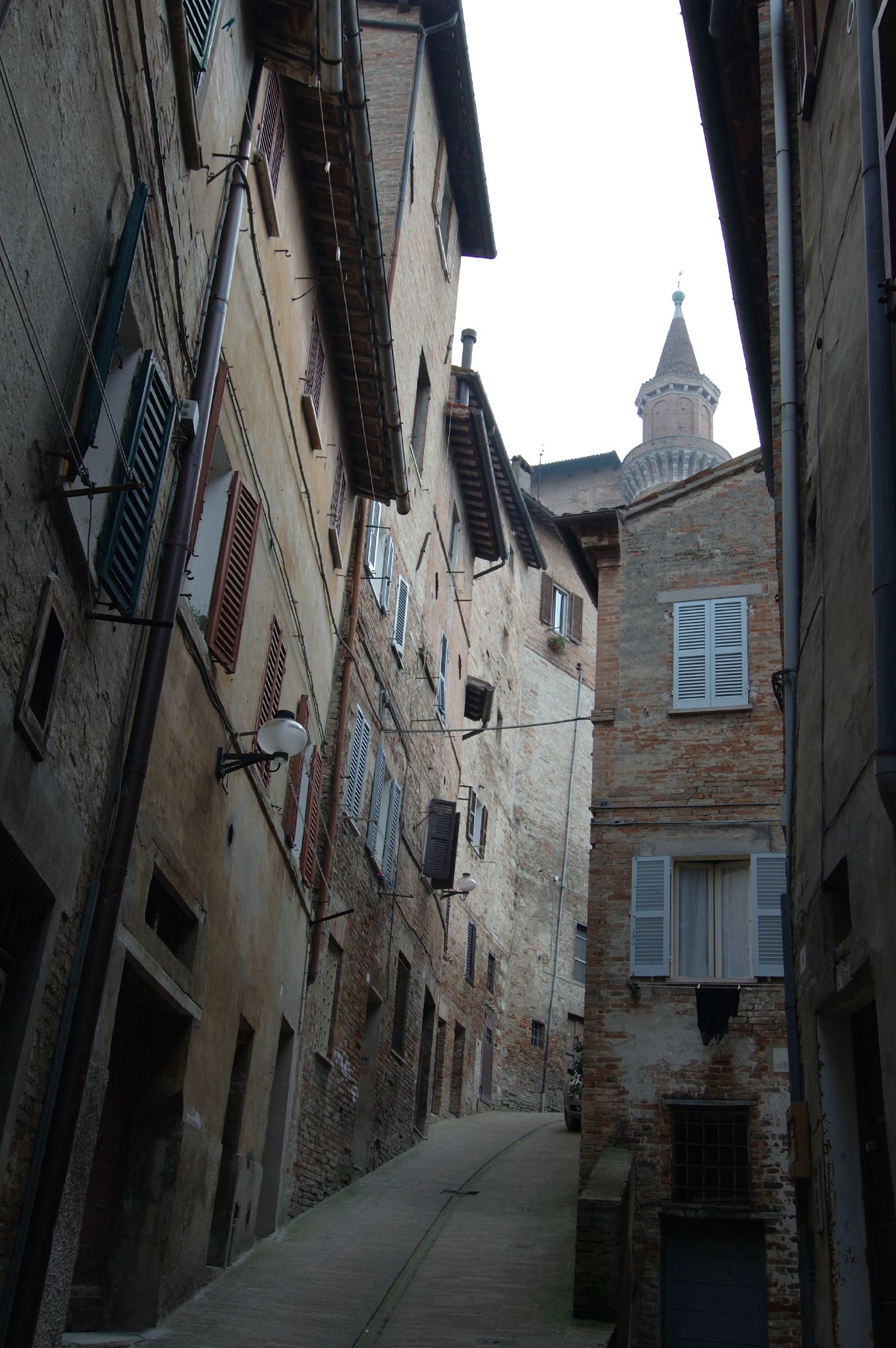 ruelle en pente du centre historique d’urbino déserte avec une tour à l’arrière-plan