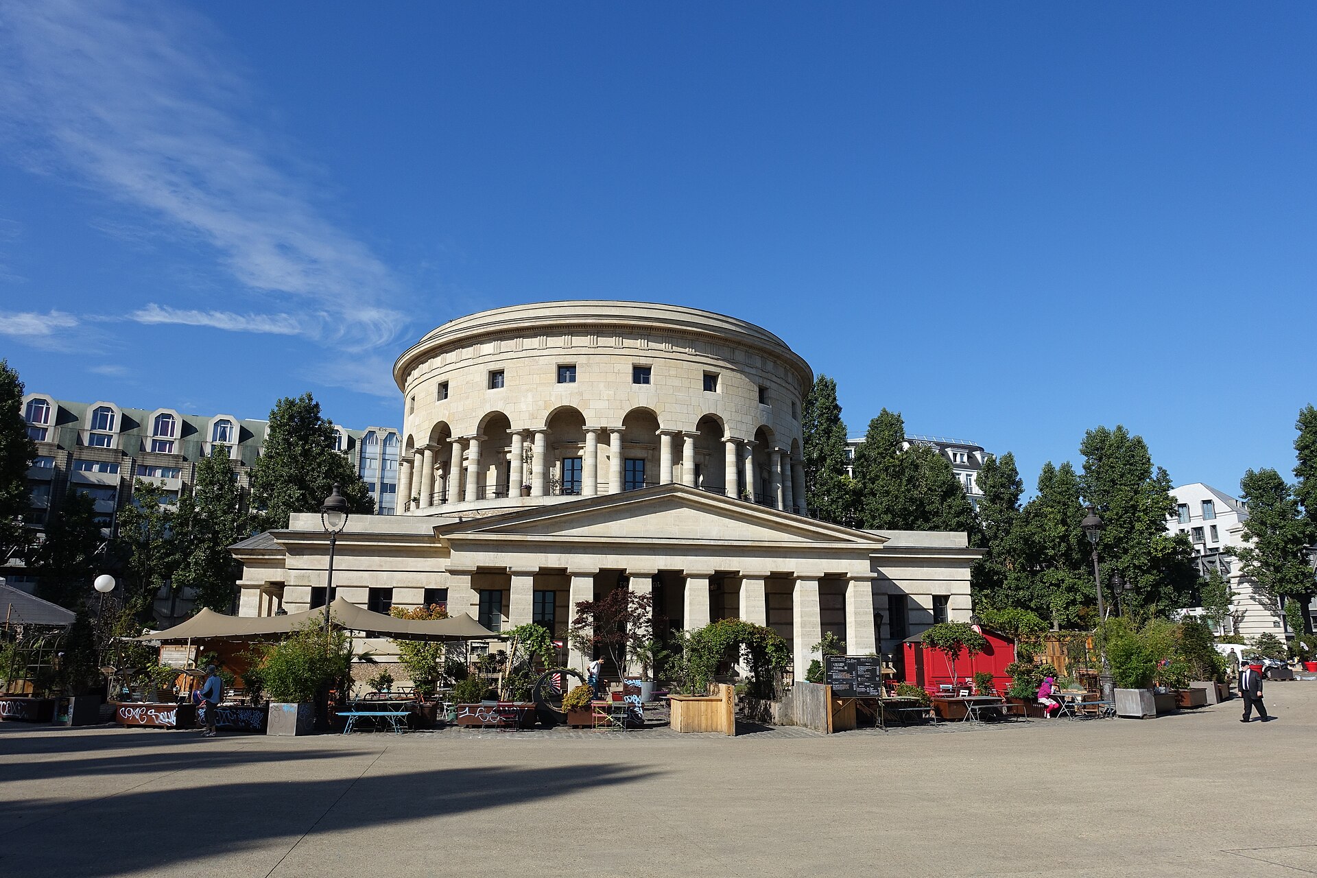 la rotonde de la villette a parigi, il tamburo cilindrico di pietra chiara sopra una galleria ad archi con colonne accoppiate e il portico con frontone triangolare, con i tavolini del ristorante davanti