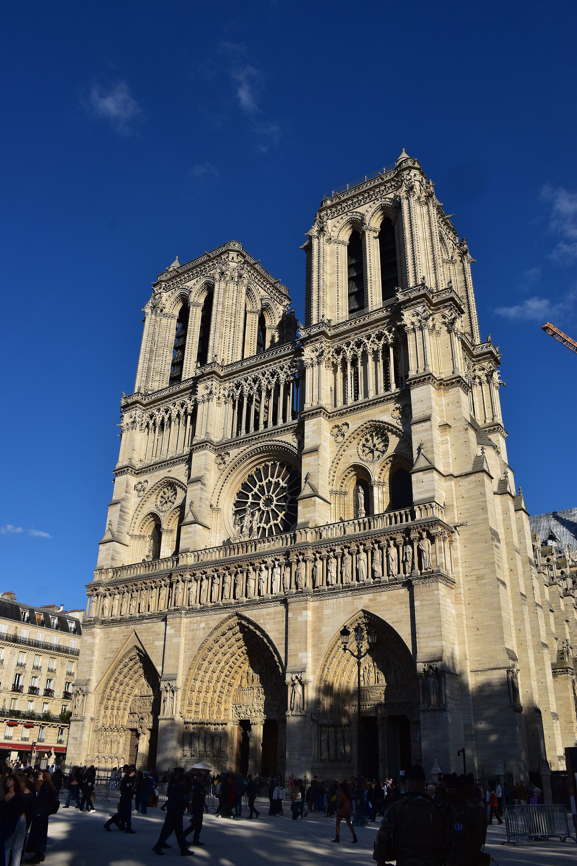 la facciata ovest di notre dame de paris dopo il restauro, la pietra chiara con i tre portali scolpiti, la fila dei re nella galleria, il rosone centrale e le due torri quadrate contro un cielo blu