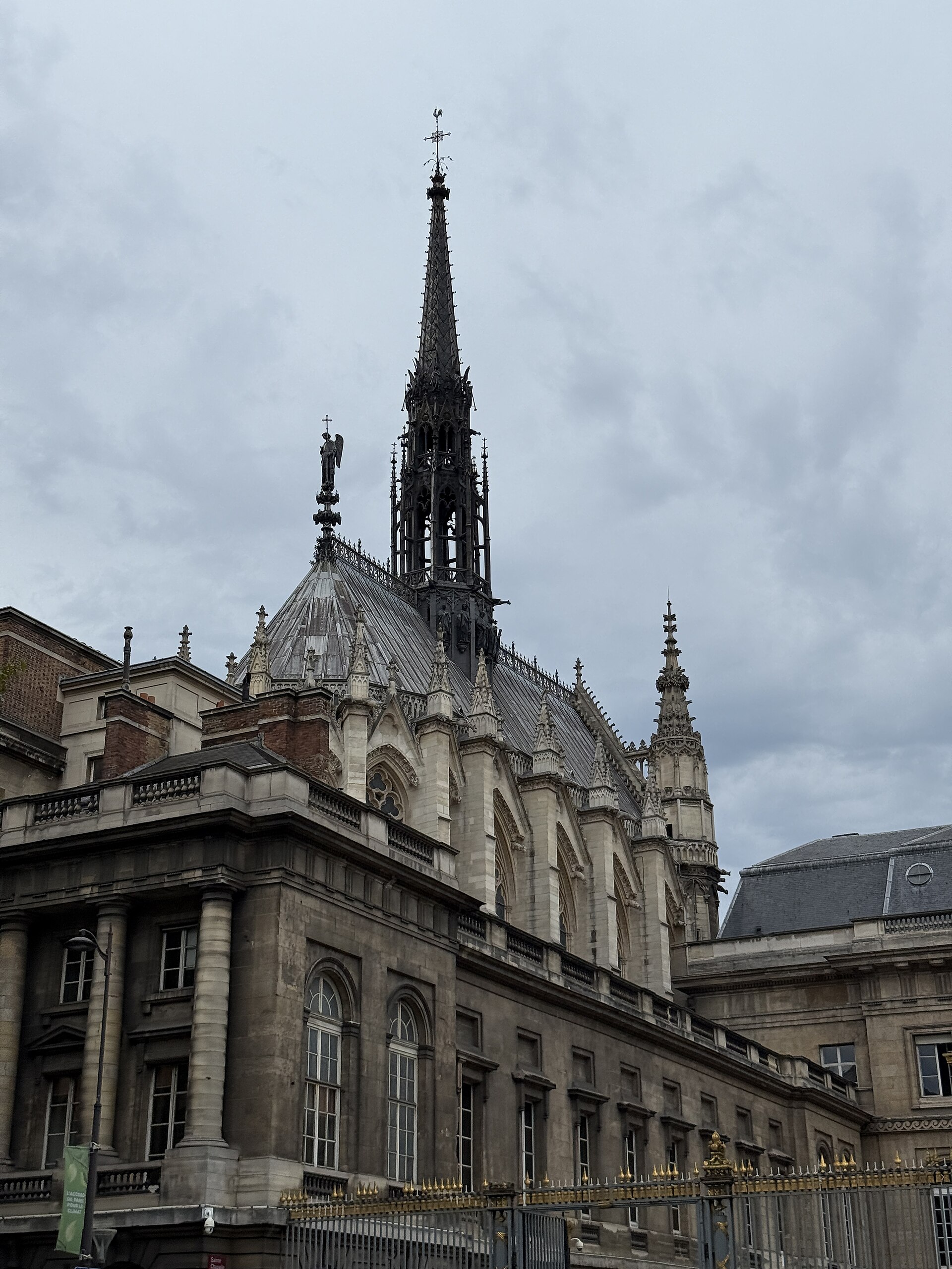 la guglia nera e il tetto a scaglie della sainte chapelle di parigi visti da fuori, sopra la facciata classica del palais de justice con le colonne e la cancellata a punte dorate