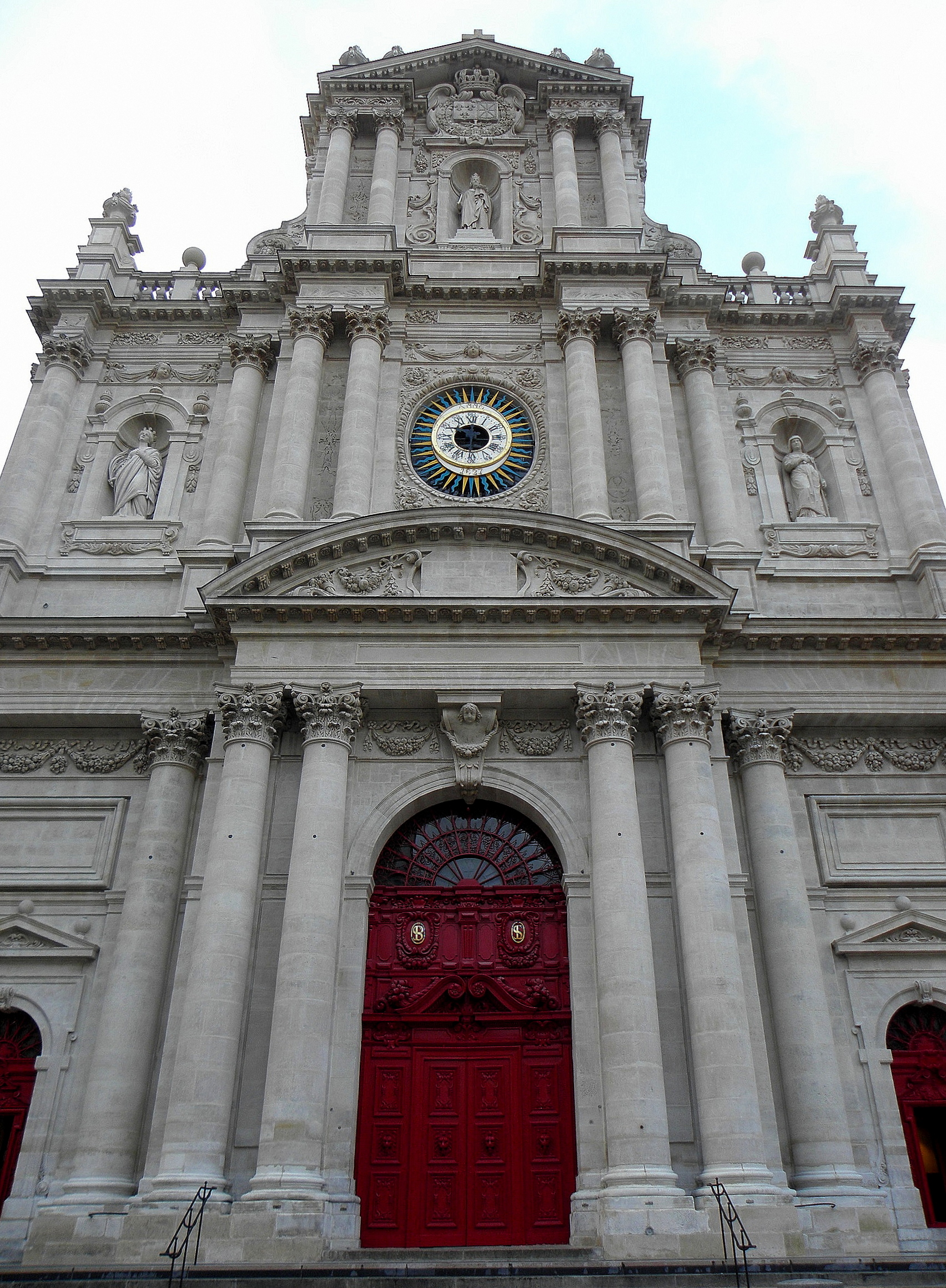 la facciata barocca della chiesa di saint paul saint louis a parigi vista dal basso, con le colonne sovrapposte, le statue nelle nicchie, il quadrante dorato e i portoni rossi