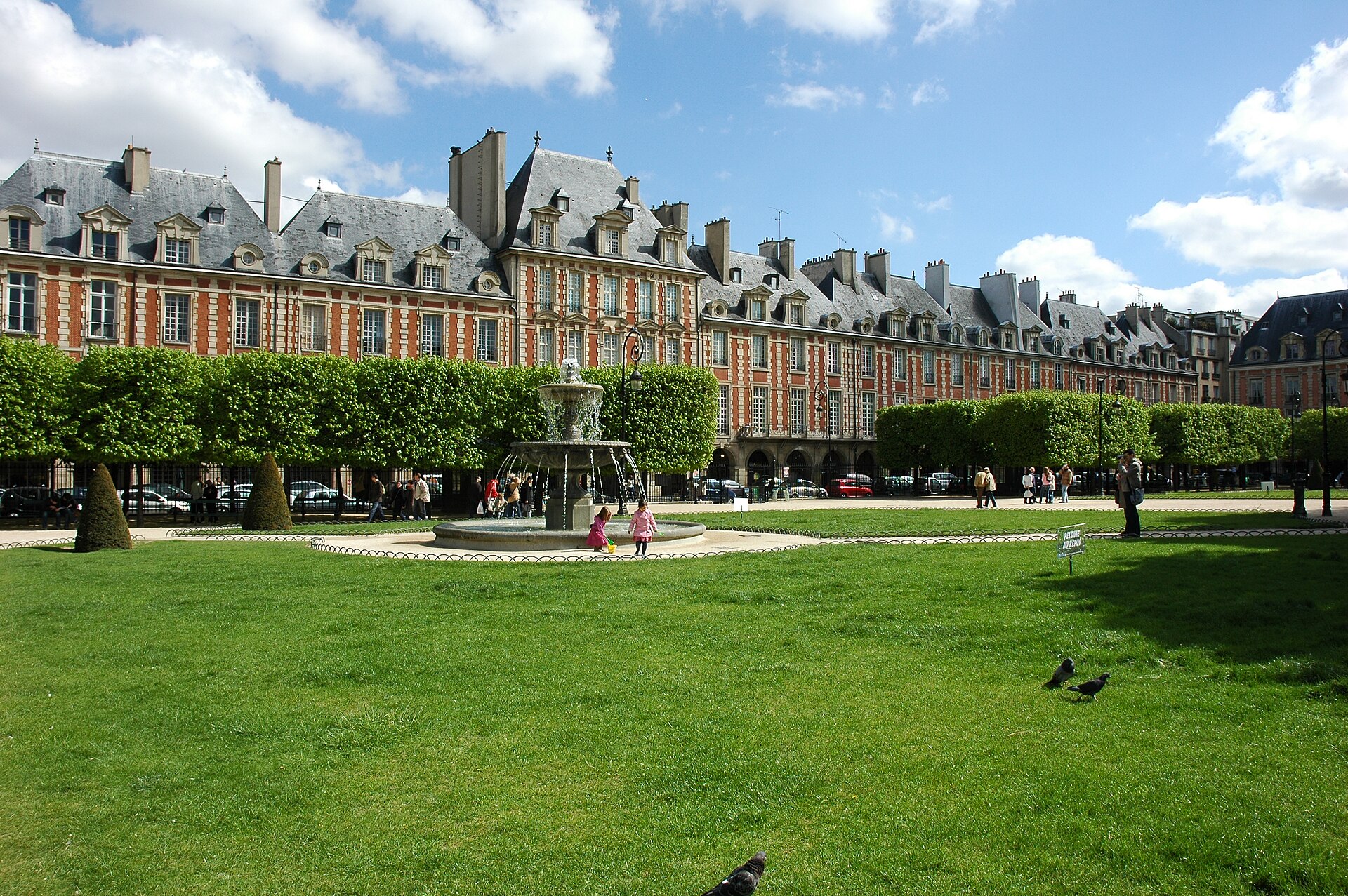 place des vosges a parigi, i padiglioni di mattone rosso e pietra chiara con i tetti d ardesia e le finestre a lucernario, una fontana di pietra e il prato del giardino in primo piano