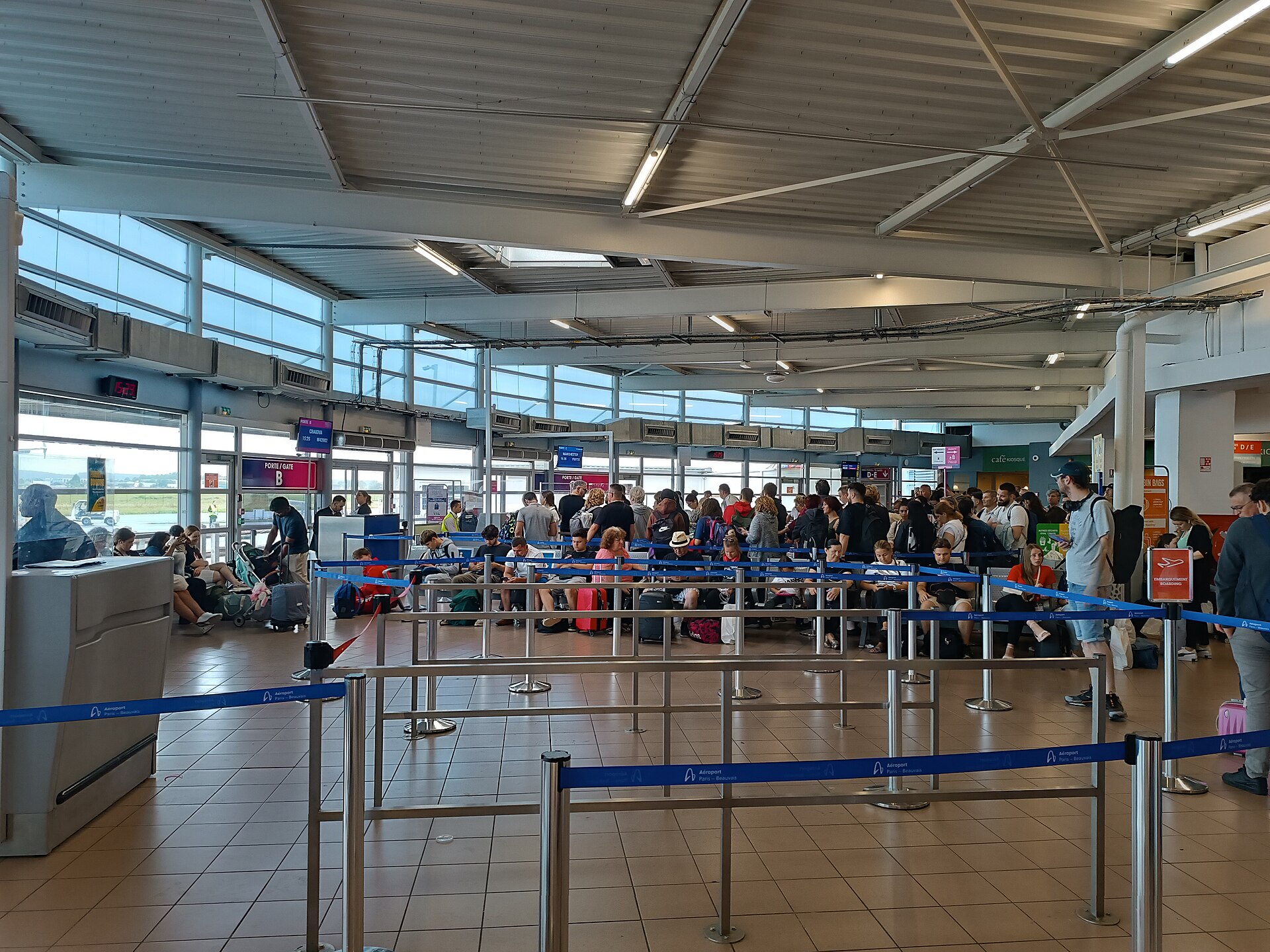 la sala d’imbarco dell’aeroporto di beauvais tille con i passeggeri in coda alla porta e i tabelloni dei voli