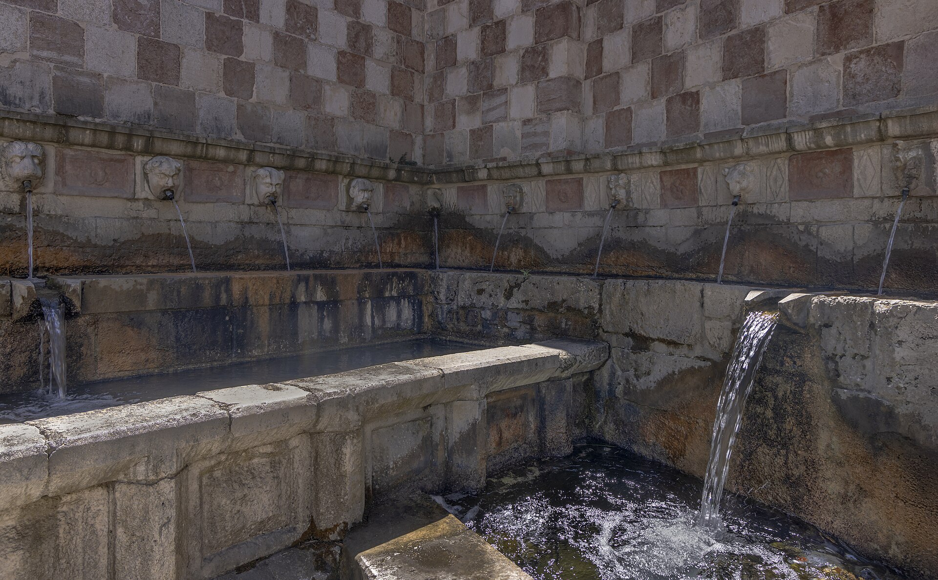 l angolo della fontana delle 99 cannelle con i mascheroni di pietra il muro a scacchi e l acqua che cade nella vasca