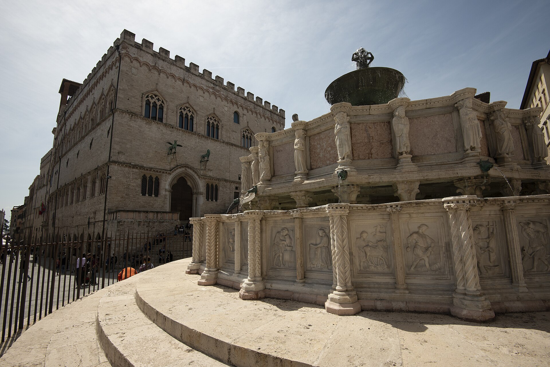 la fontana maggiore di perugia vista di tre quarti con i rilievi delle vasche e il palazzo dei priori dietro